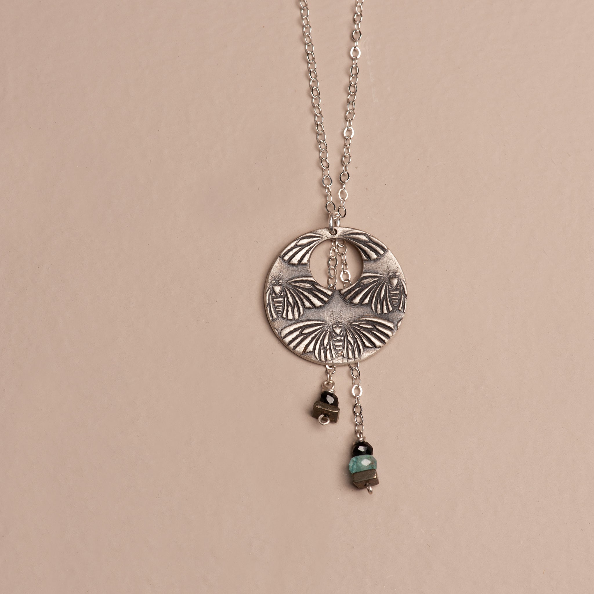 Oxidized sterling silver crescent moon pendant with multiple moth figures and cascading drops of cool-toned aquamarine, black tourmaline, and square pyrite gemstones.