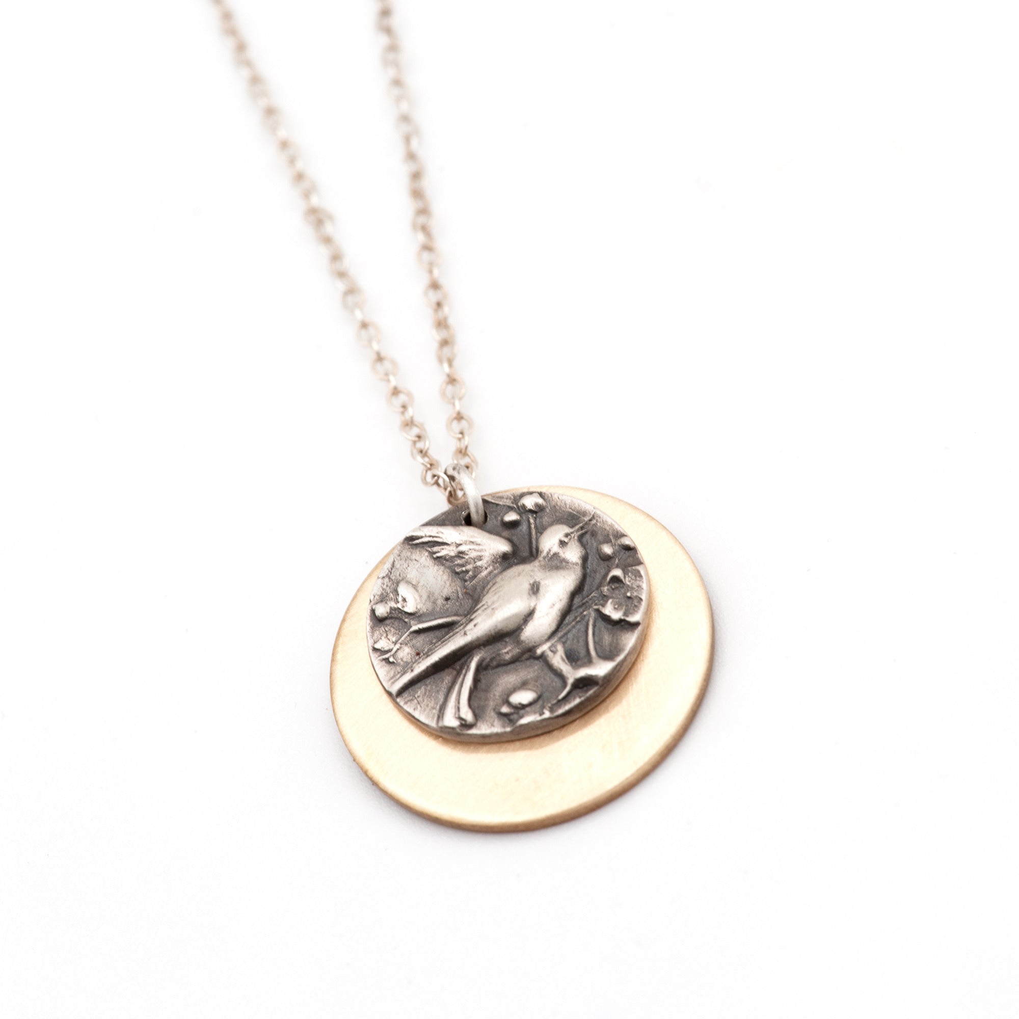 Close up of Birds of Flutter handcrafted silver bird charm pressed from vintage button mold on bronze disc, by Jester Swink