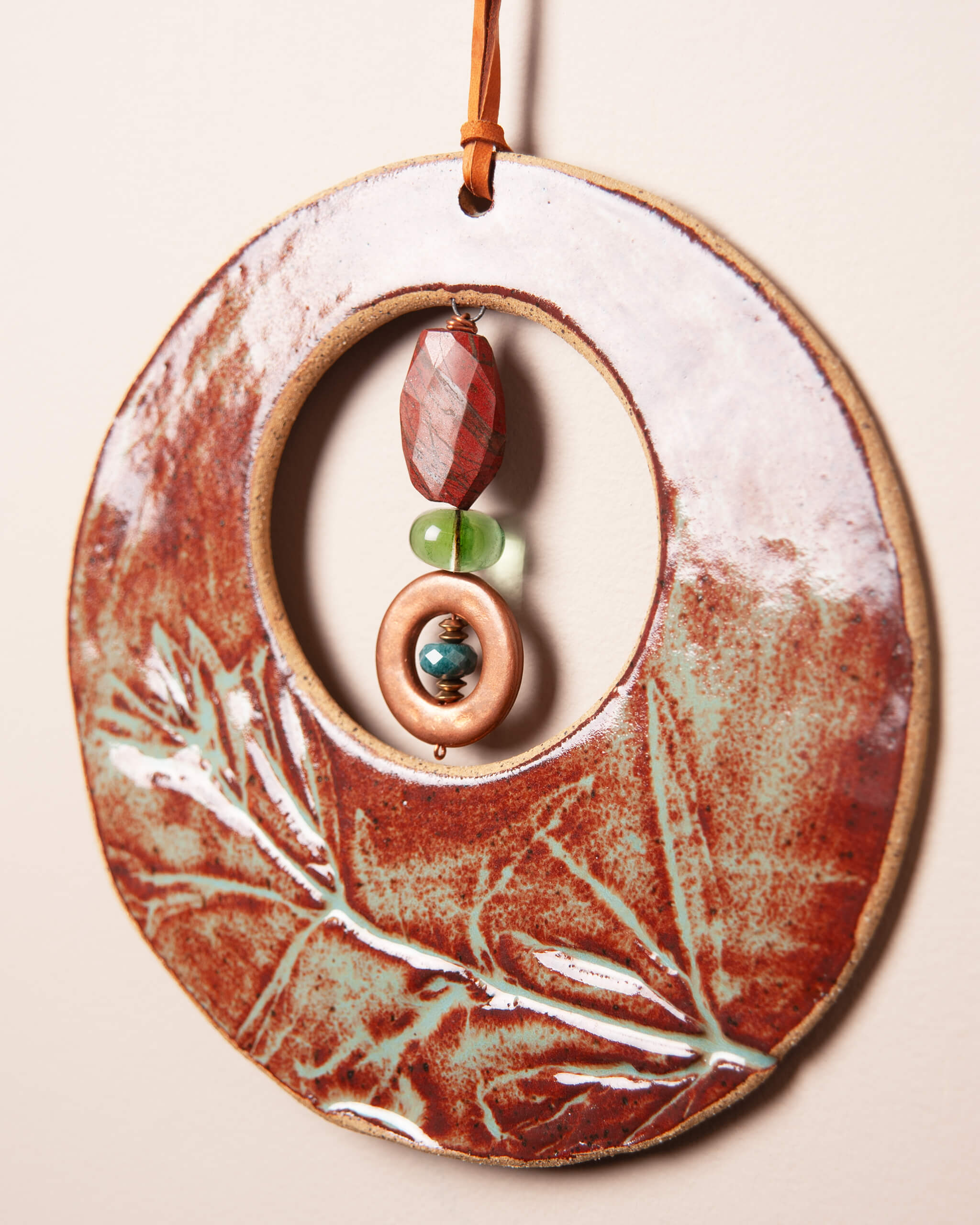 Close up of wildflower impression in rusty orange glazed river rock ceramic clay with jasper, fluorite and green onyx stone stack