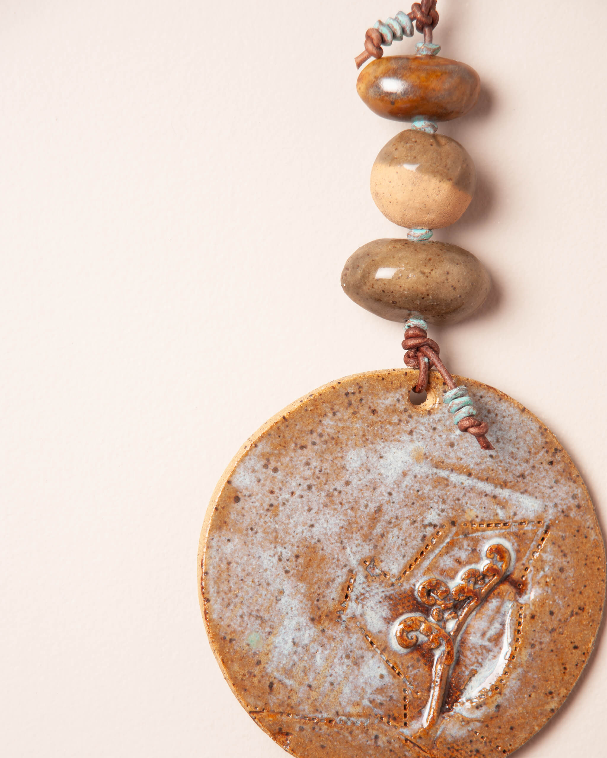 Close up of river rock ceramic bead stack showing flat backed forms and round center bead with dark brown leather and patinated brass detail