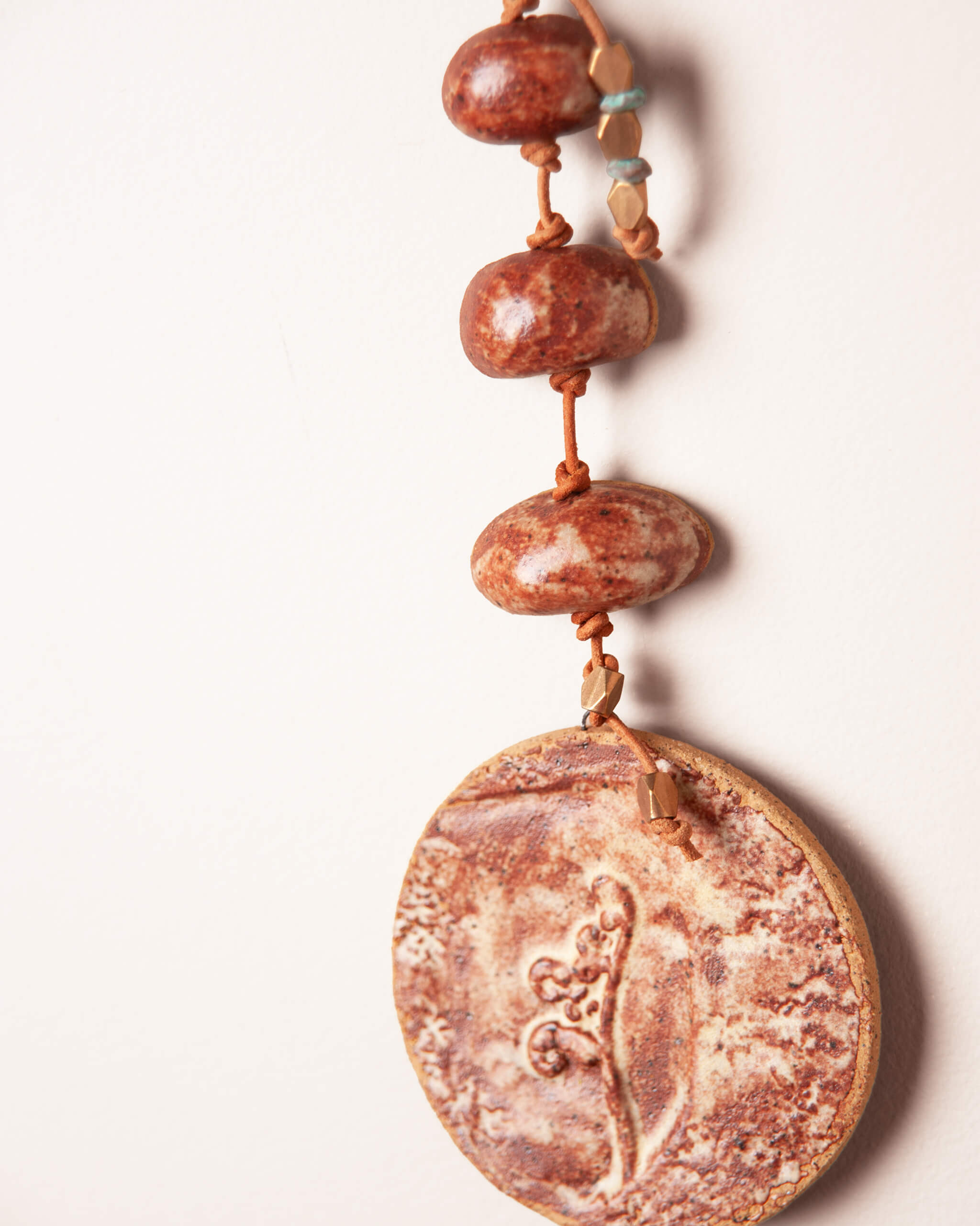 Close up of raised fiddlehead fern impression on terracotta glazed ceramic disc with patinated brass and bronze accent beads