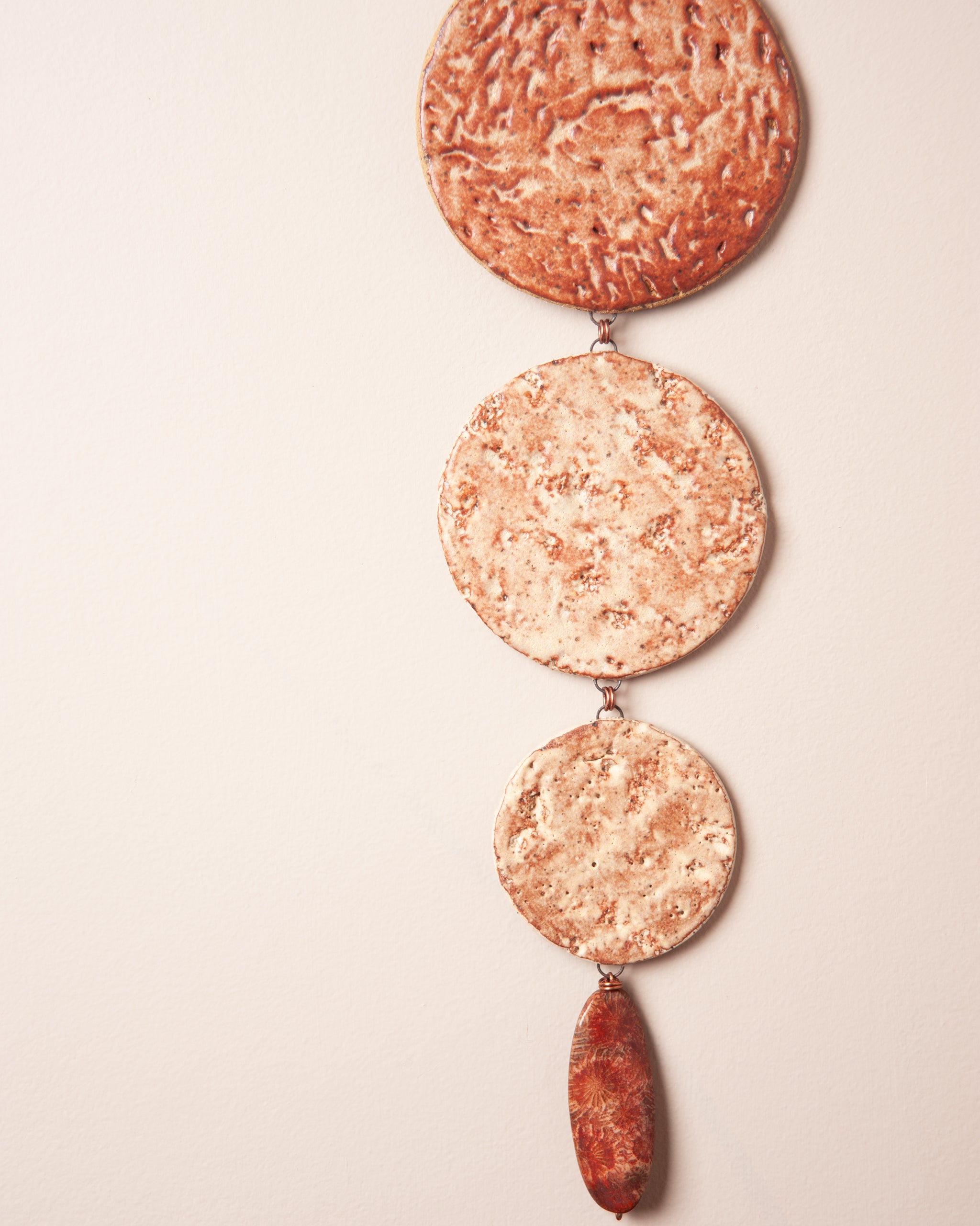 Close up of graduating ceramic discs with redwood bark impression and copper jump ring connections with fossilized coral agate drop