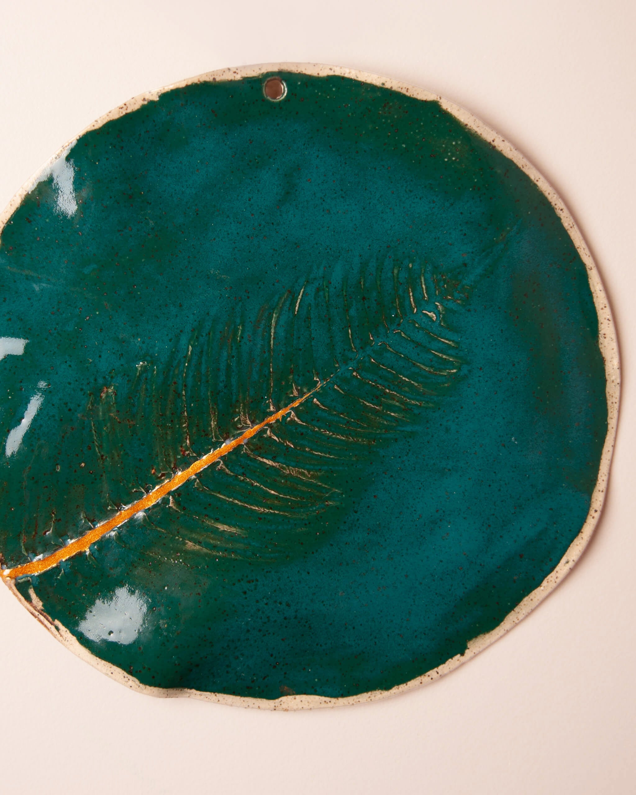 Close up of fern impression in emerald glazed white speckled ceramic clay showing kintsugi gold line running diagonally across Golden Fern plaque