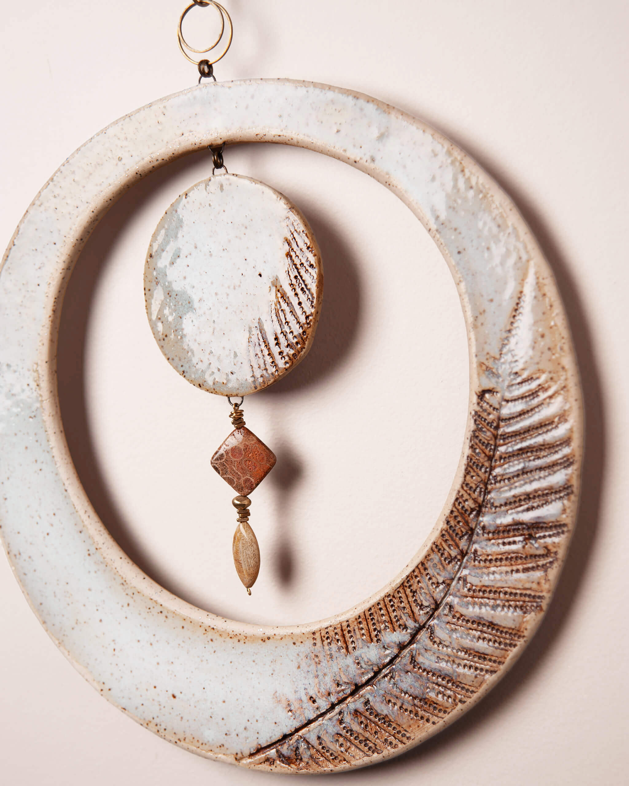 Close up of fern impression in ice blue glazed ceramic clay with fossilized coral agate wire wrap and copper diamond charm