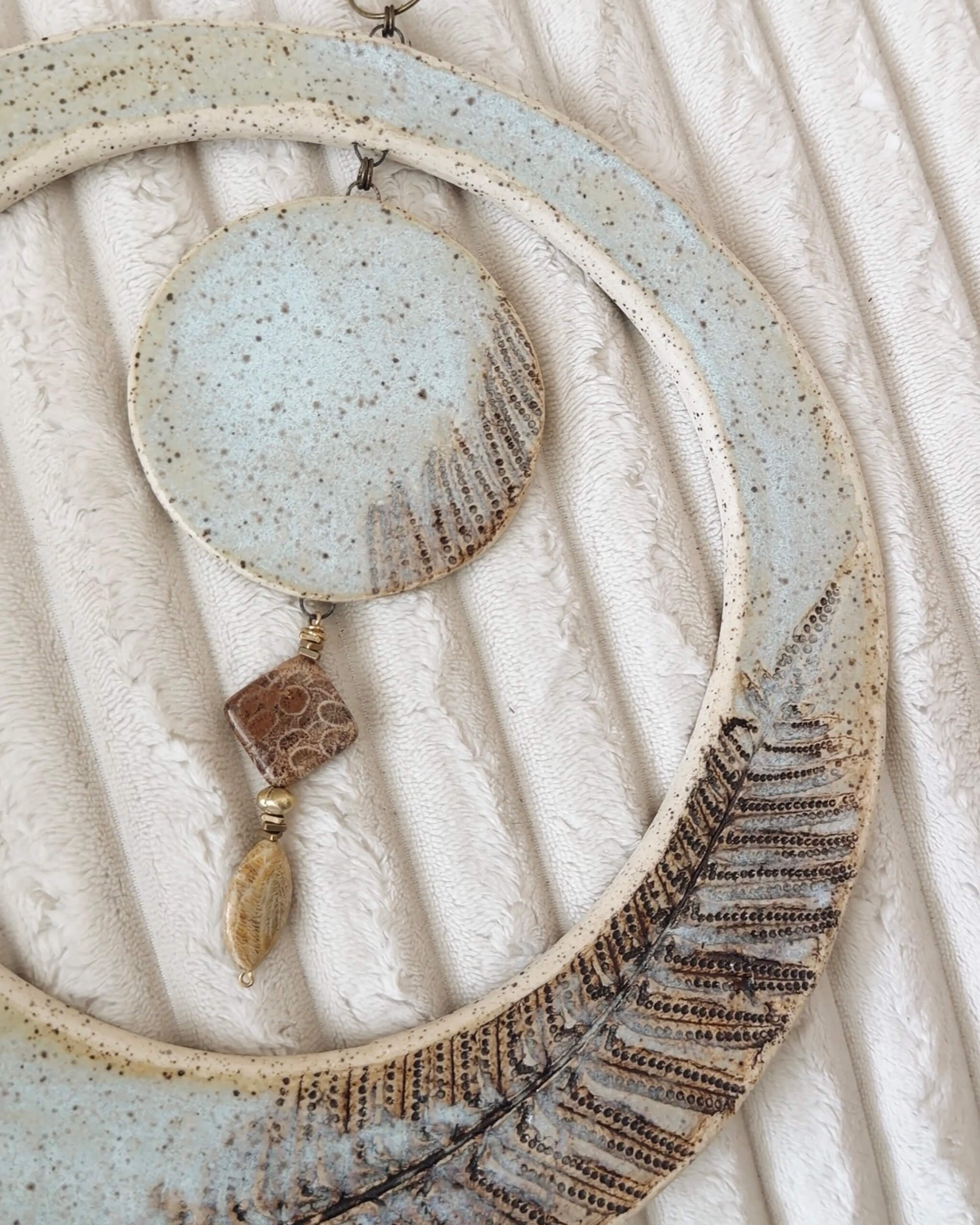 Lunar Fern large handmade ceramic wall art resting on plush fabric loveseat showing full scale and ice blue glaze detail