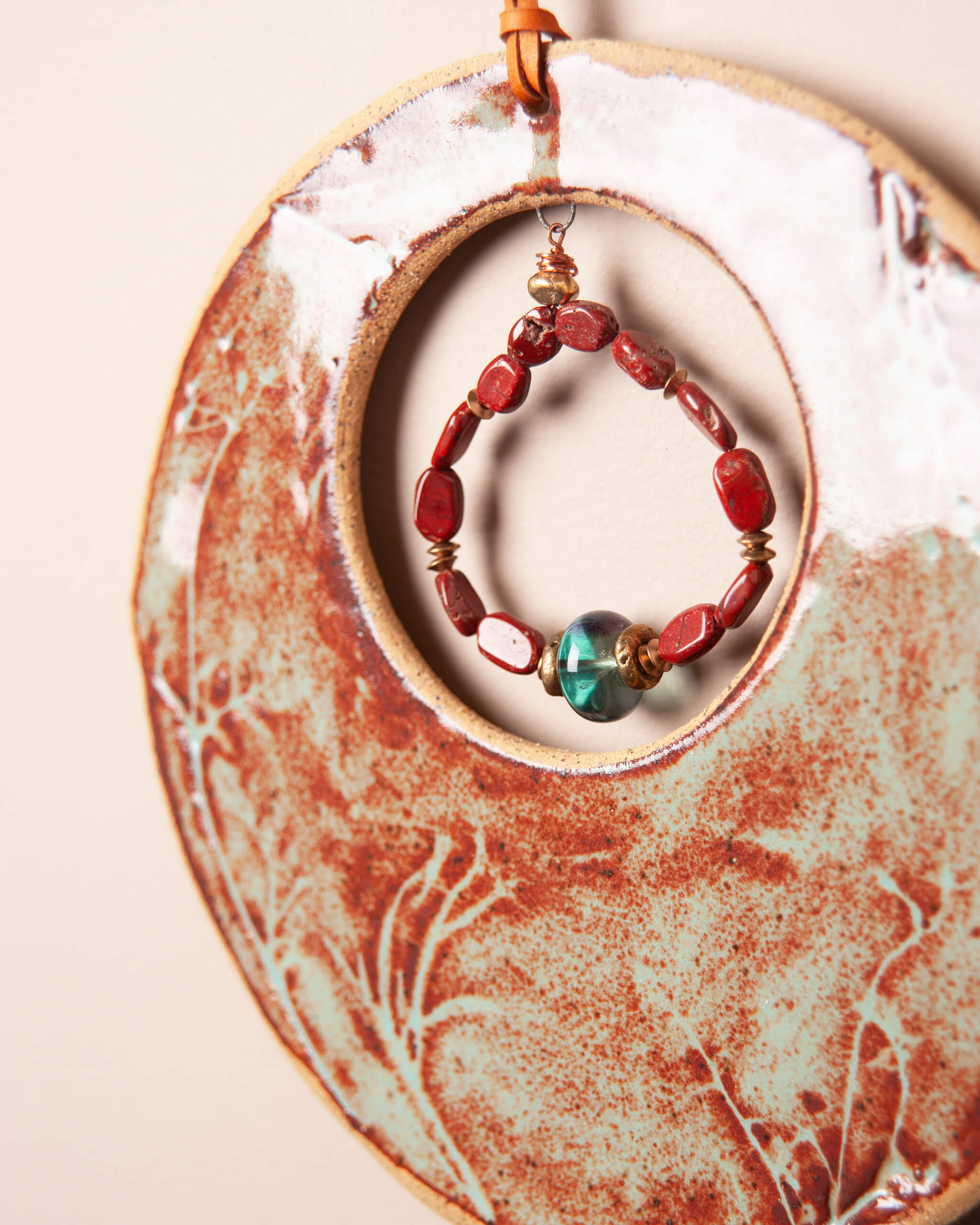 Close up of wildflower impression in sandy speckled ceramic clay with red jasper and fluorite strand and brass accents