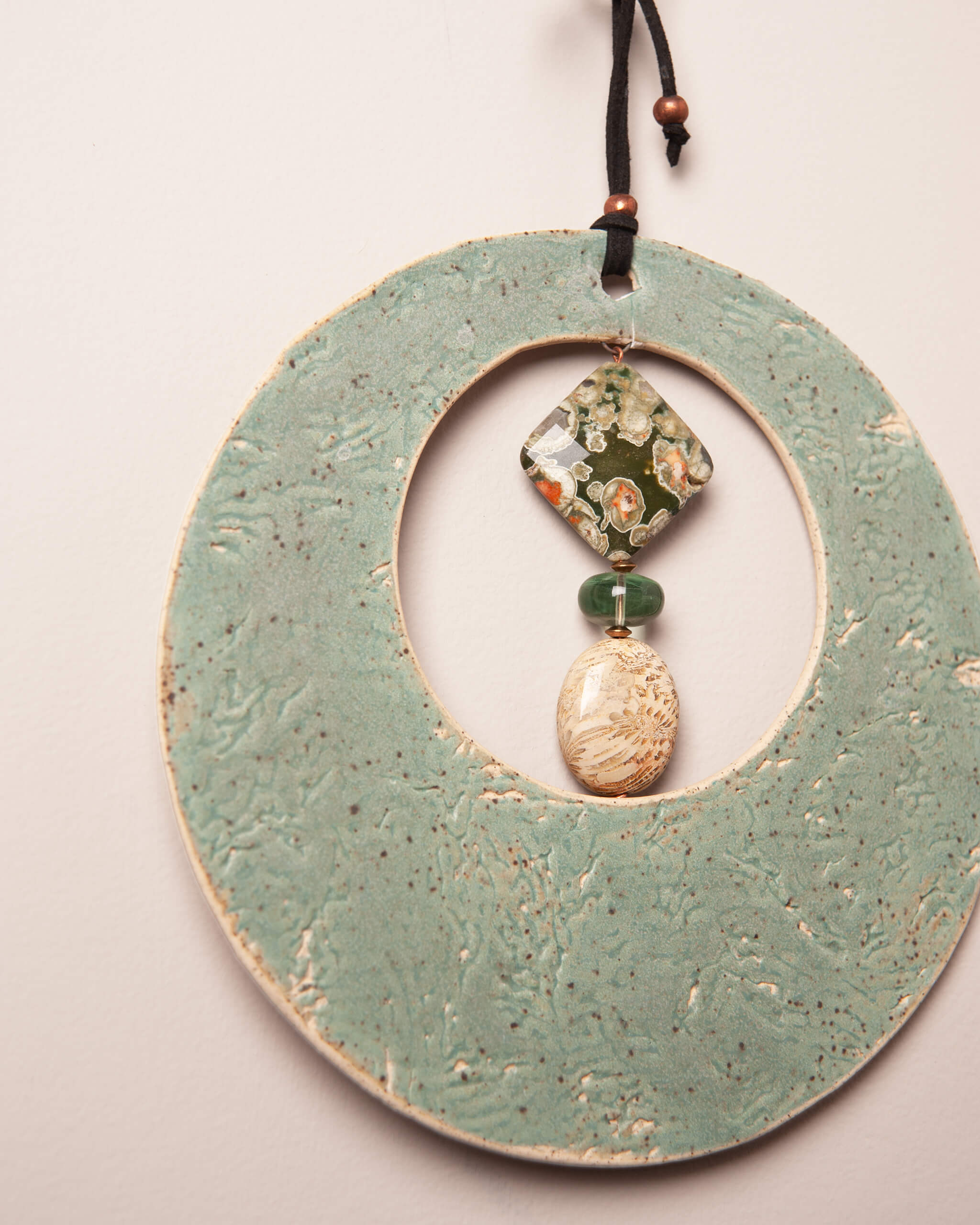 Close up of sea kelp texture impression in seafoam glazed white speckled ceramic clay with ocean jasper and fossilized coral agate pendant