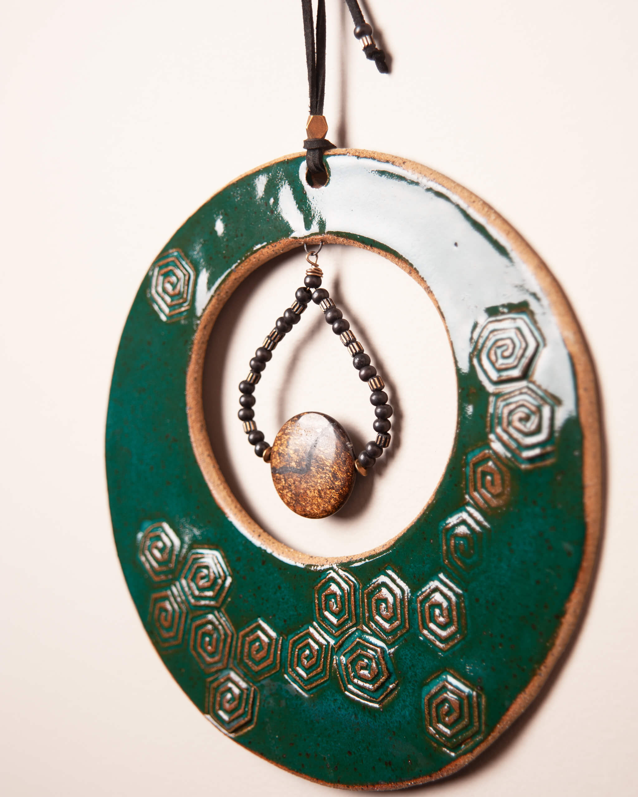 Close up of spiral hex pattern impression in emerald green glazed sandy speckled ceramic clay with bronzite and brass bead teardrop pendant