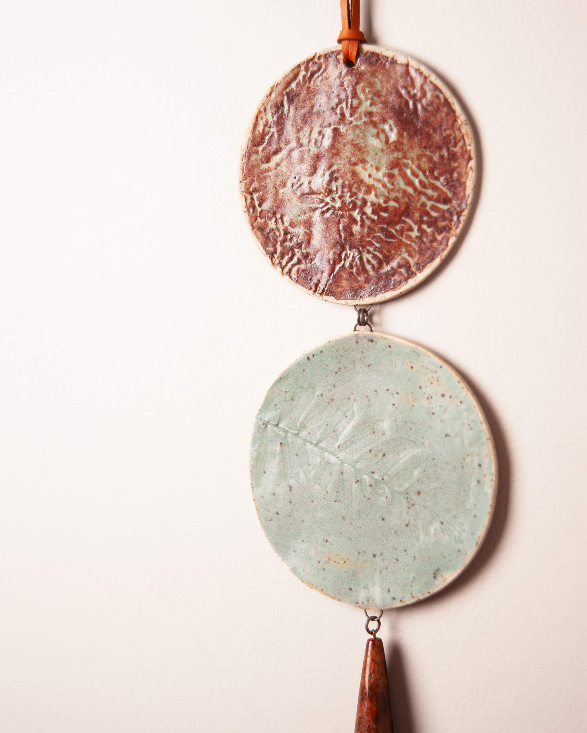 Close up of sea kelp impression in rusty terracotta glazed ceramic disc and fern impression in seafoam glazed ceramic disc with fossilized coral agate drop