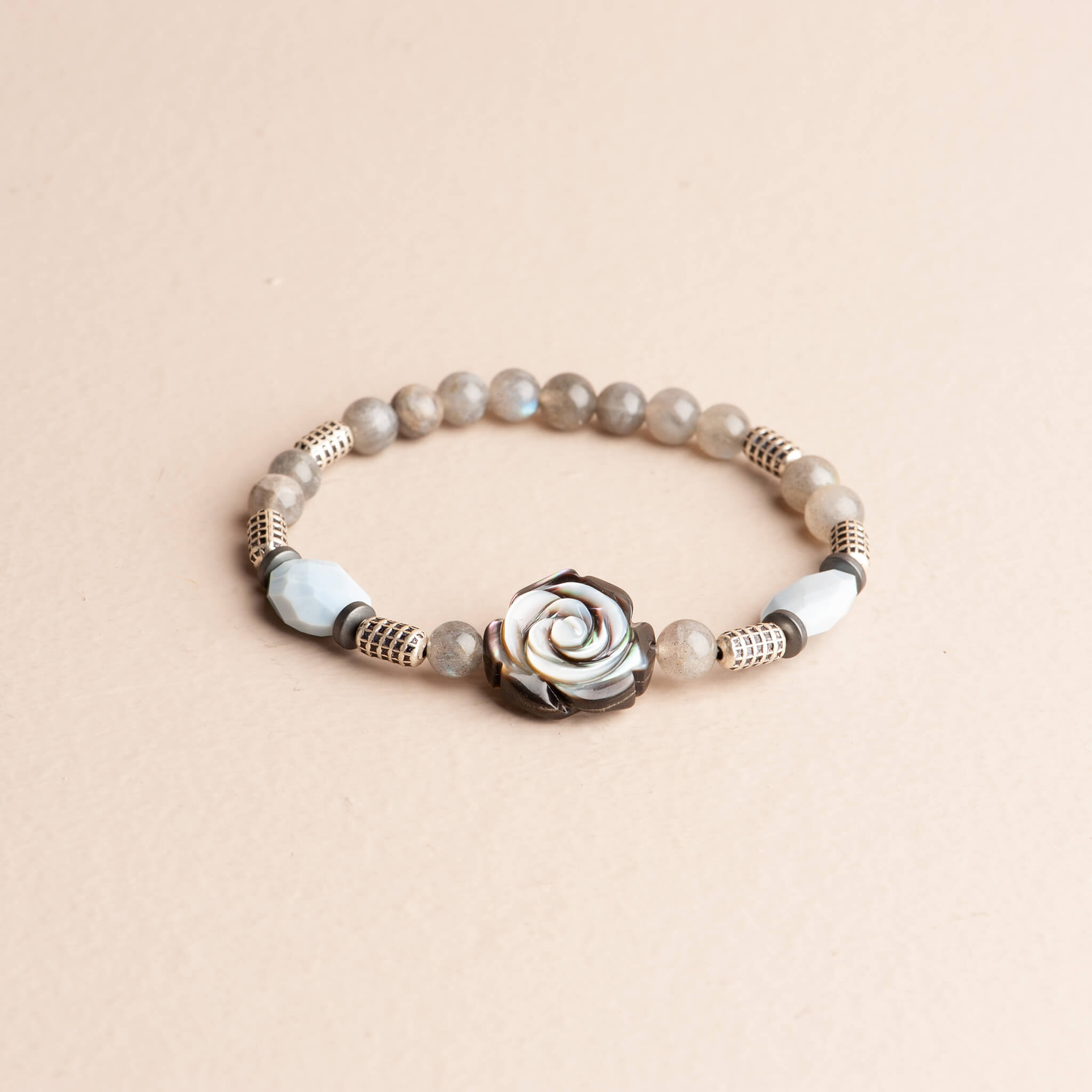 Stretch bracelet featuring a central carved abalone shell flower, smooth grey labradorite beads, light blue faceted blue lace agate, and silver plated spacers.