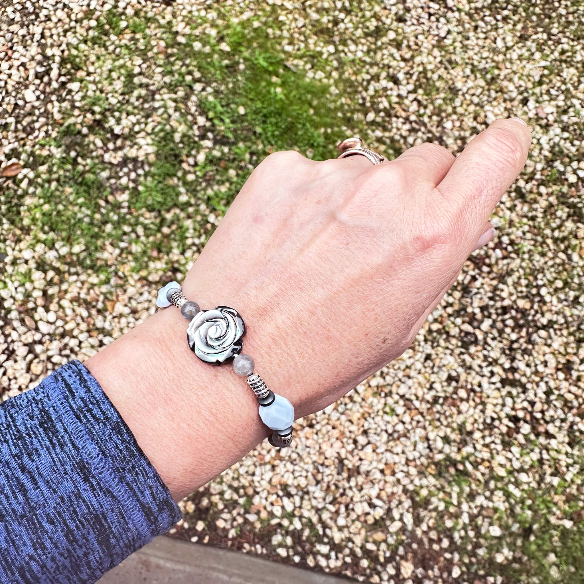 The Bloom Bracelet with abalone shell flower focal piece worn on a woman's wrist outdoors over a blue shirt, emphasizing the scale of the charm.