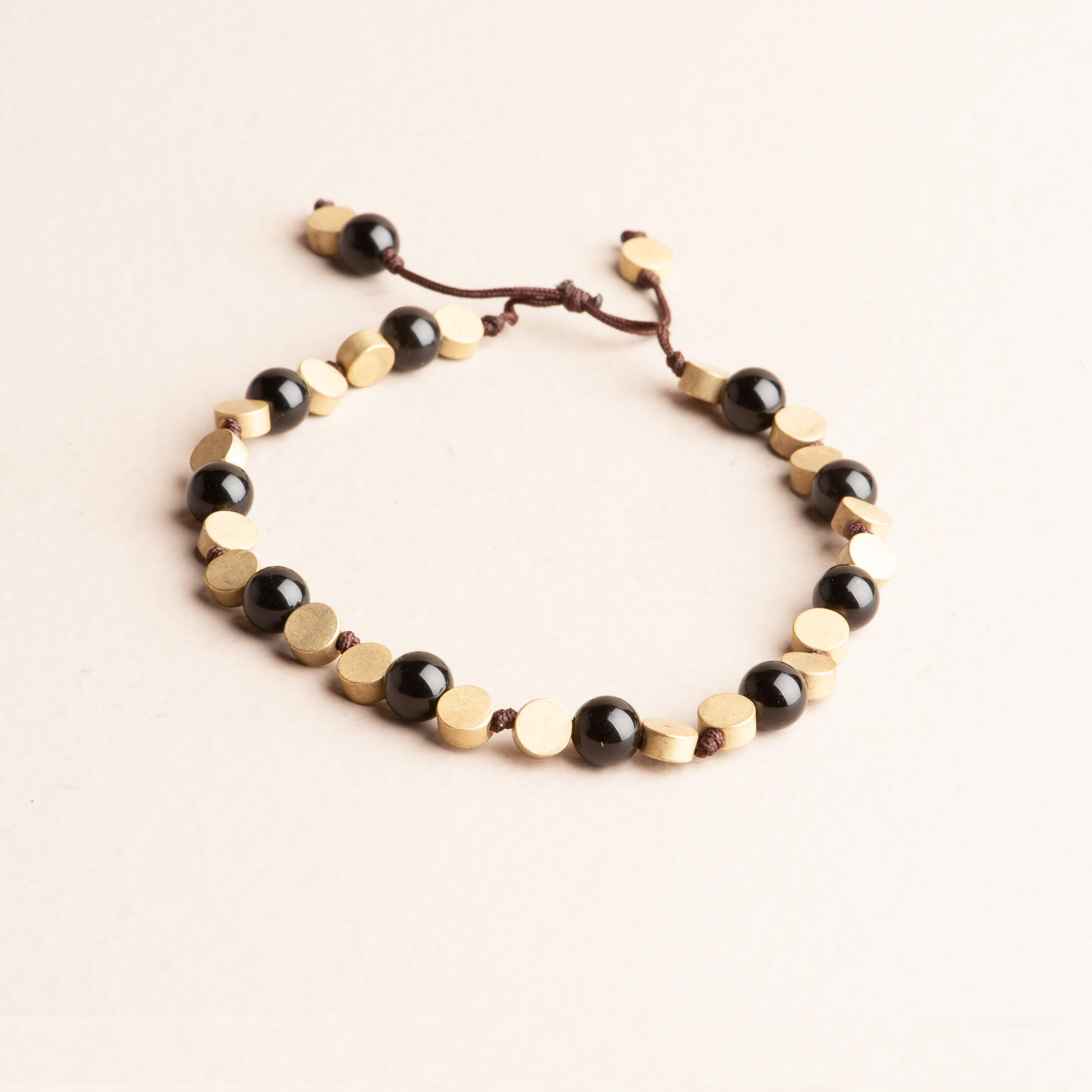 Modern Boho adjustable cord bracelet featuring alternating polished black obsidian beads and flat round brass disc beads on a brown cord.