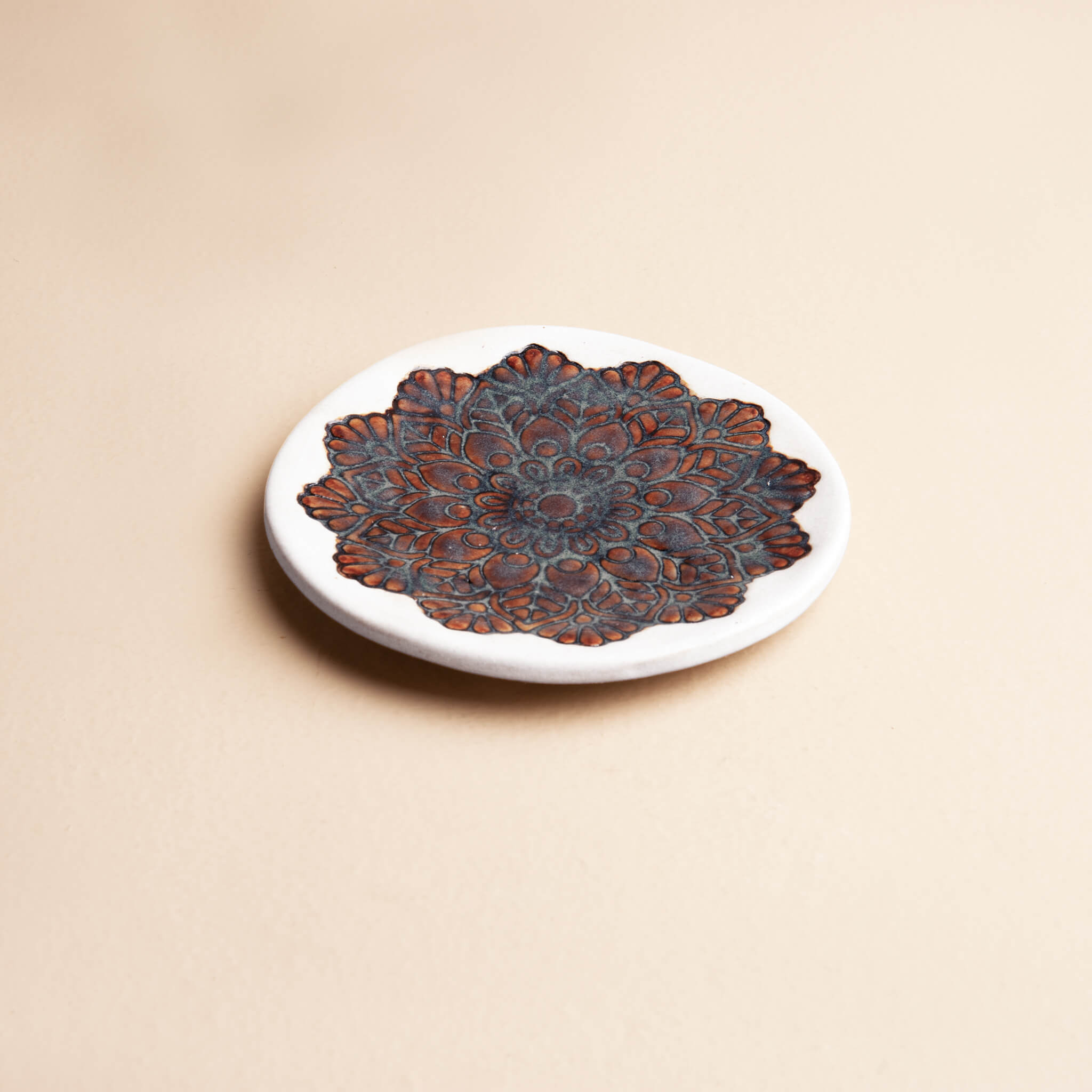 Side view of a handcrafted white clay ring dish showing the contrast between the matte white rim and the shiny, textured mandala glaze.