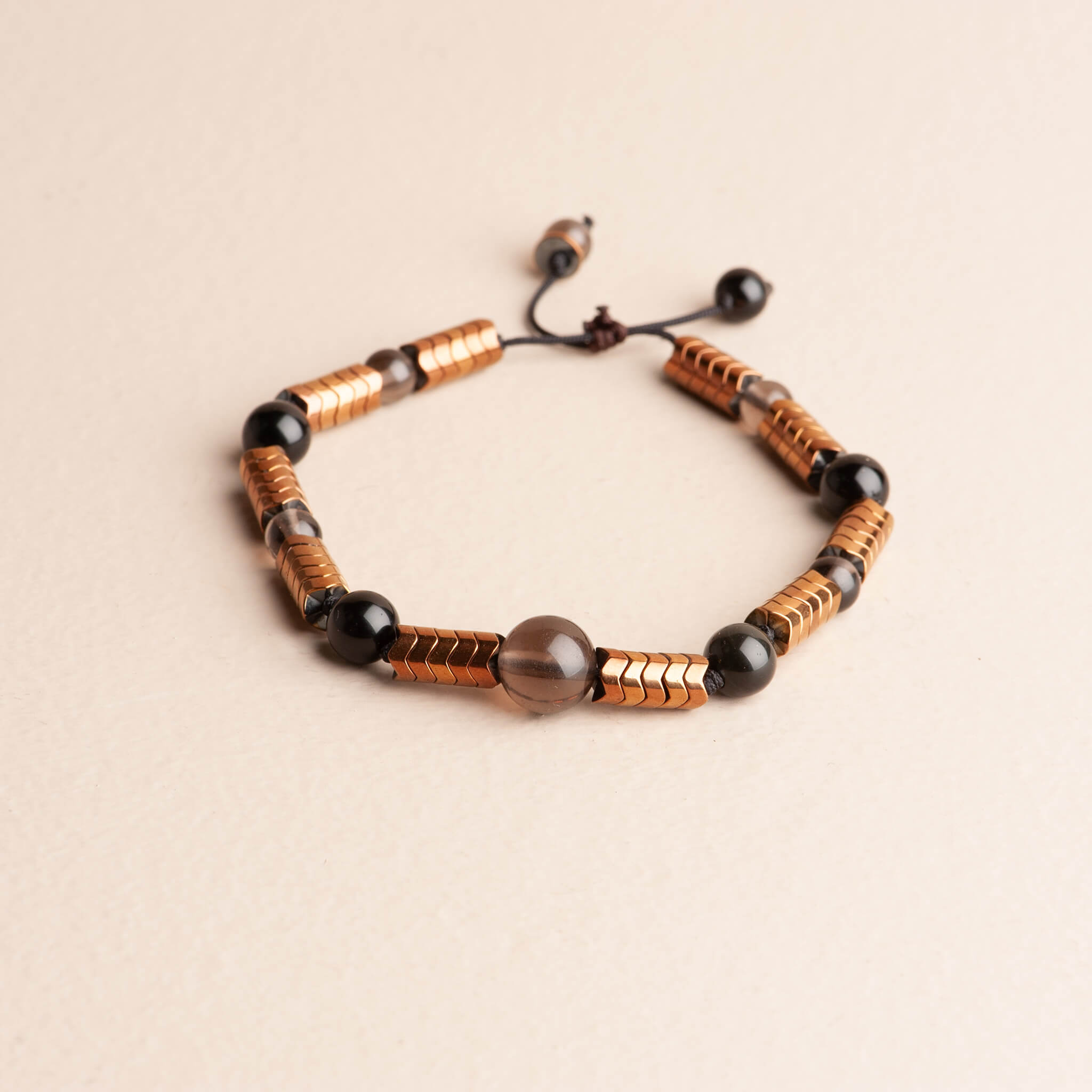 Adjustable men's beaded bracelet featuring large copper-plated hematite bar spacers, round black obsidian beads, and clear smoky quartz beads on a black cord.