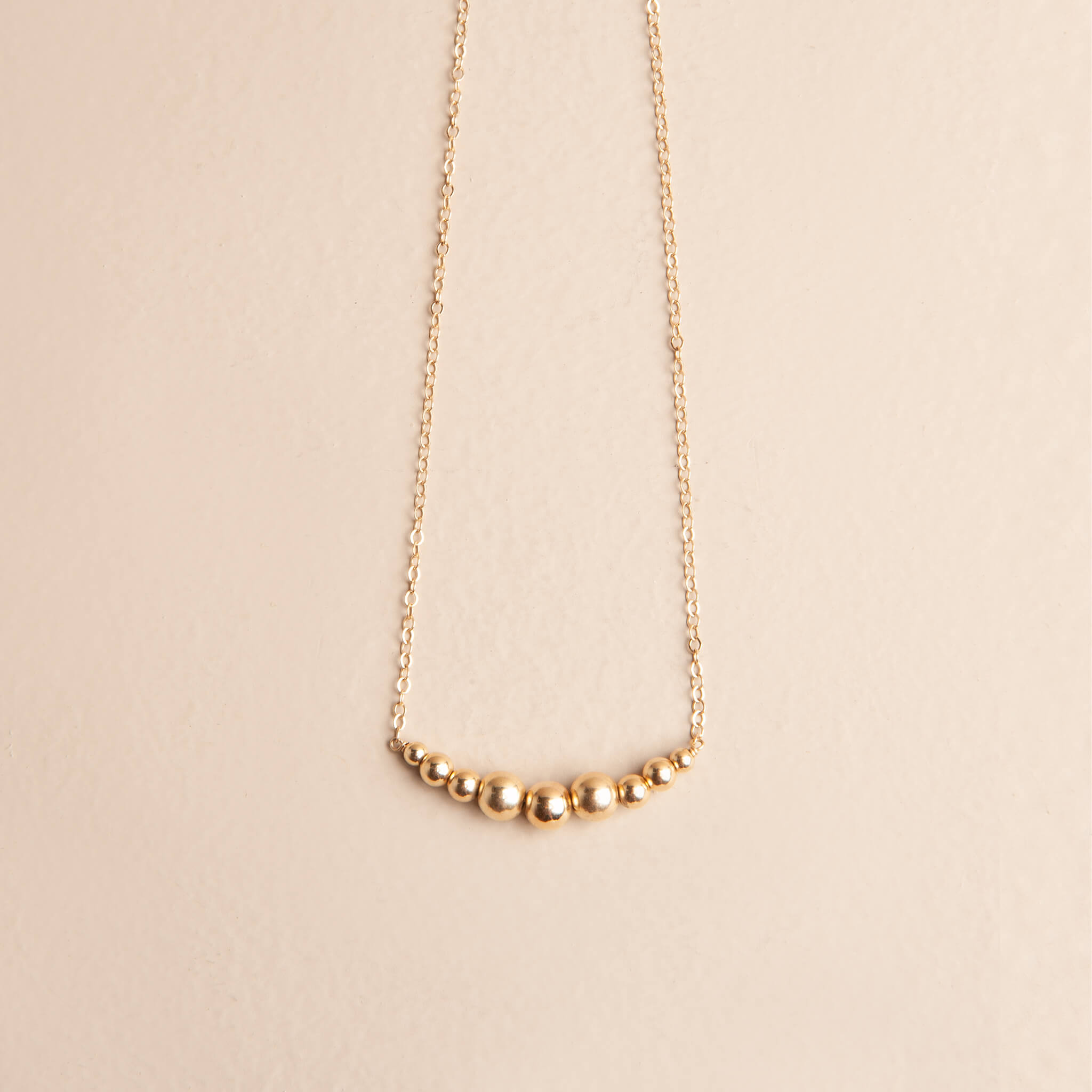 The Zenith Necklace worn by a model, showing the 14K gold fill graduating ball design worn at 18 inches, styled as a layering piece.