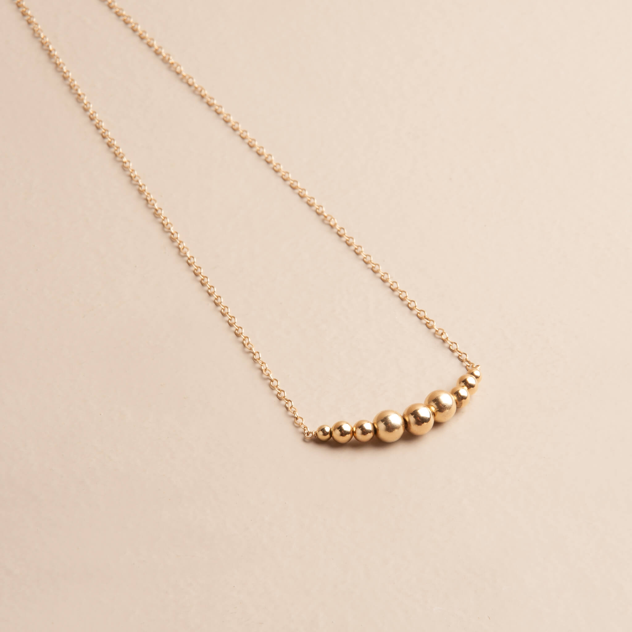 Angled close-up of The Zenith Necklace, featuring nine graduating 14K gold fill ball beads on a delicate gold chain, showcasing the subtle curve and shine.
