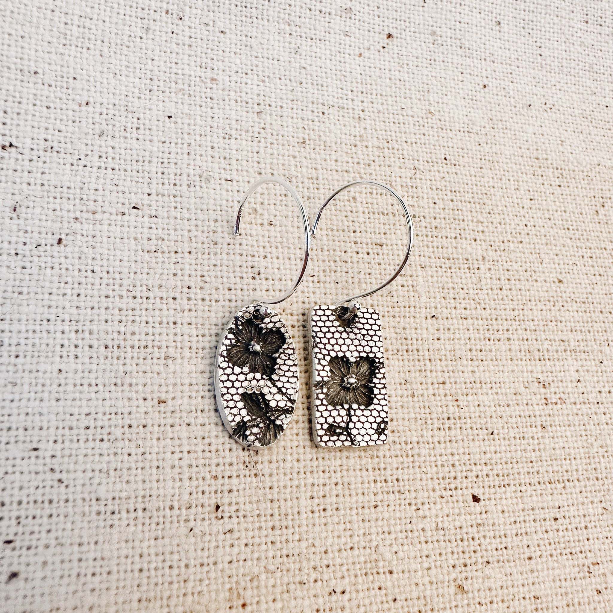 Close-up of real lace texture pressed into sterling silver on linen โ handmade dangle earrings by Jester Swink