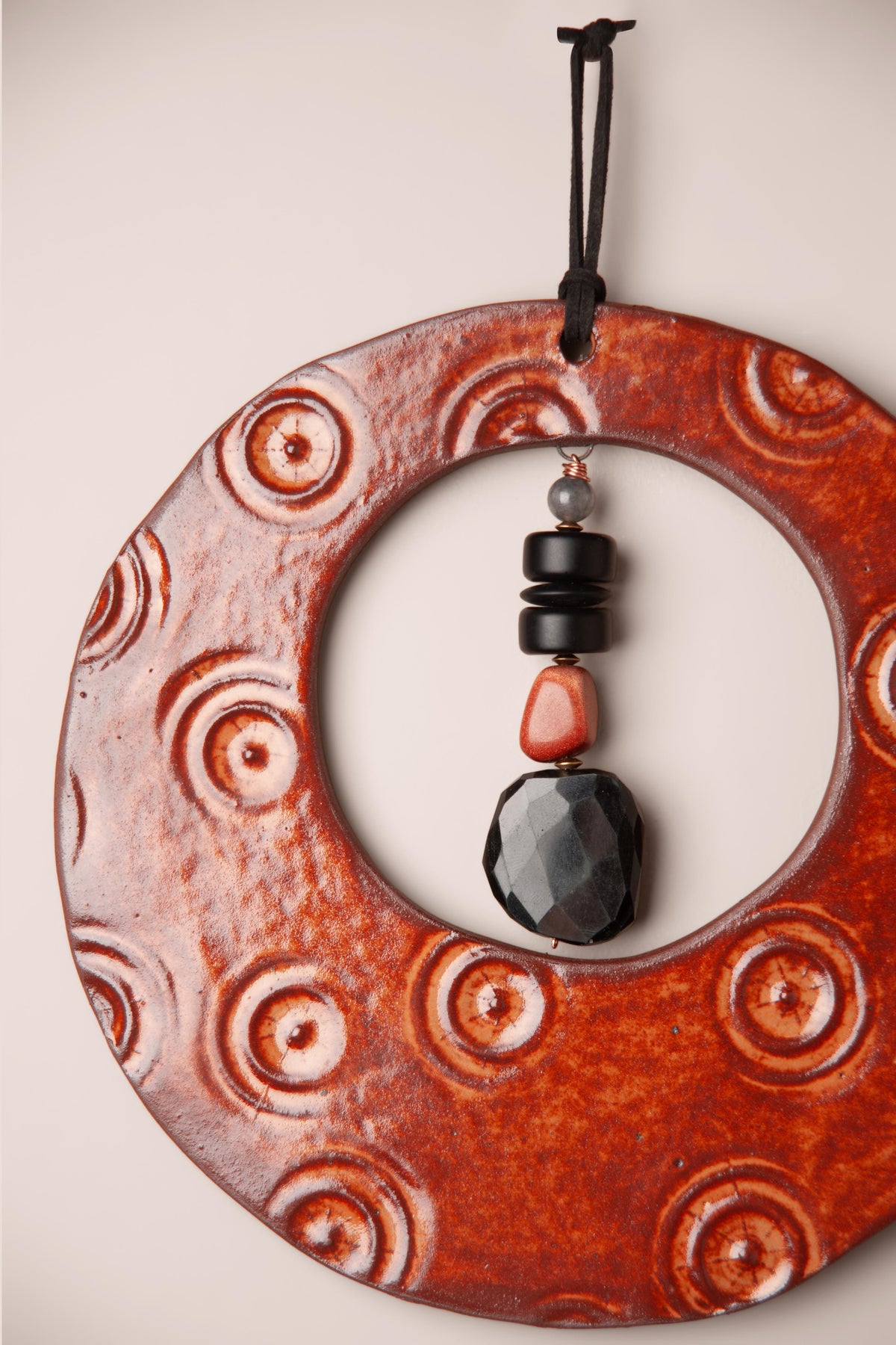 Detail of the pressed circles and stone dangle on a large handmade round ceramic wall hanging in Oolong glaze, kiln fired by Jester Swink, Santa Cruz Mountains California