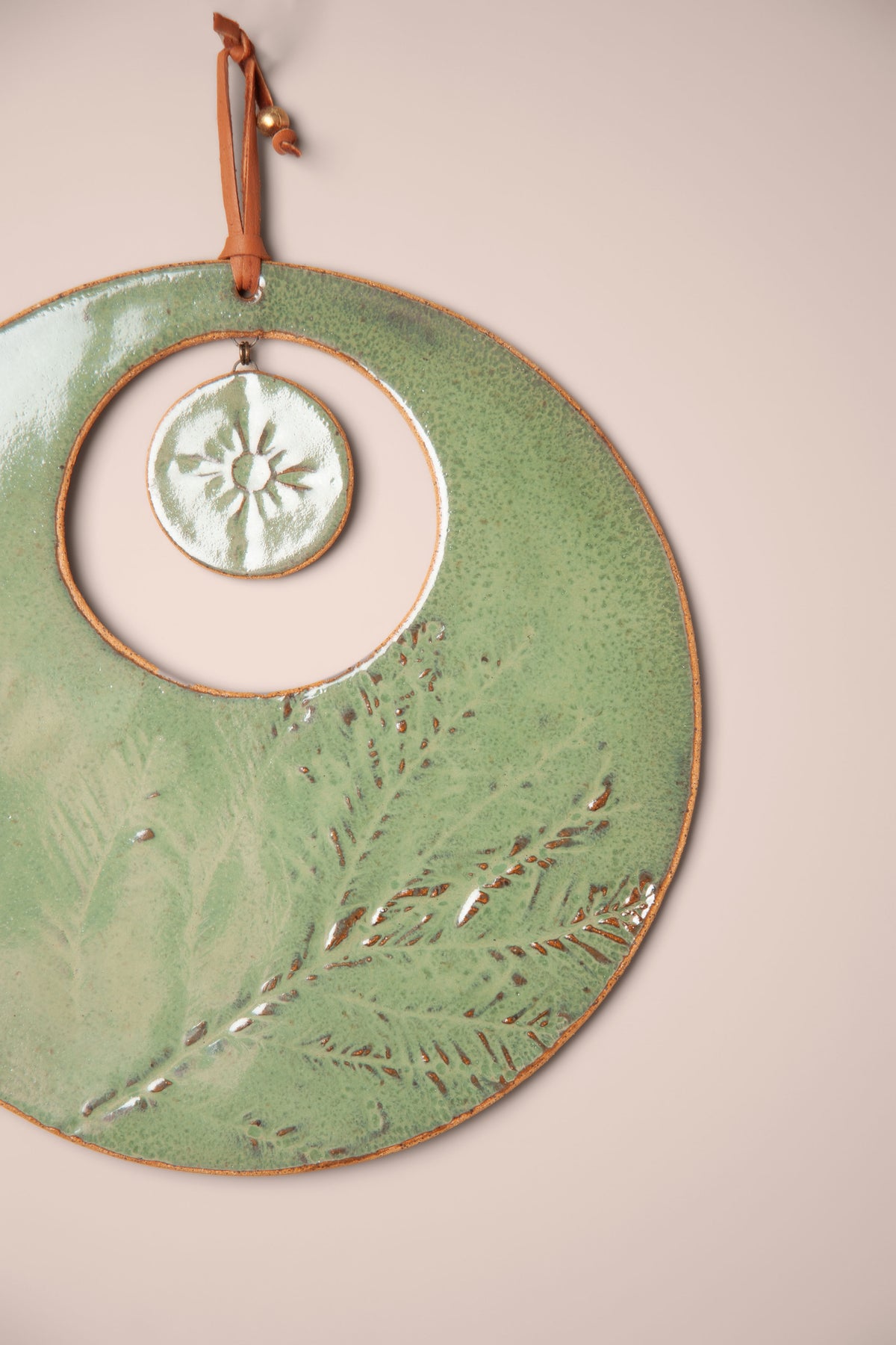 Detail of the pressed redwood needles and sun on a large handmade round ceramic wall hanging, kiln fired by Jester Swink, Santa Cruz Mountains California