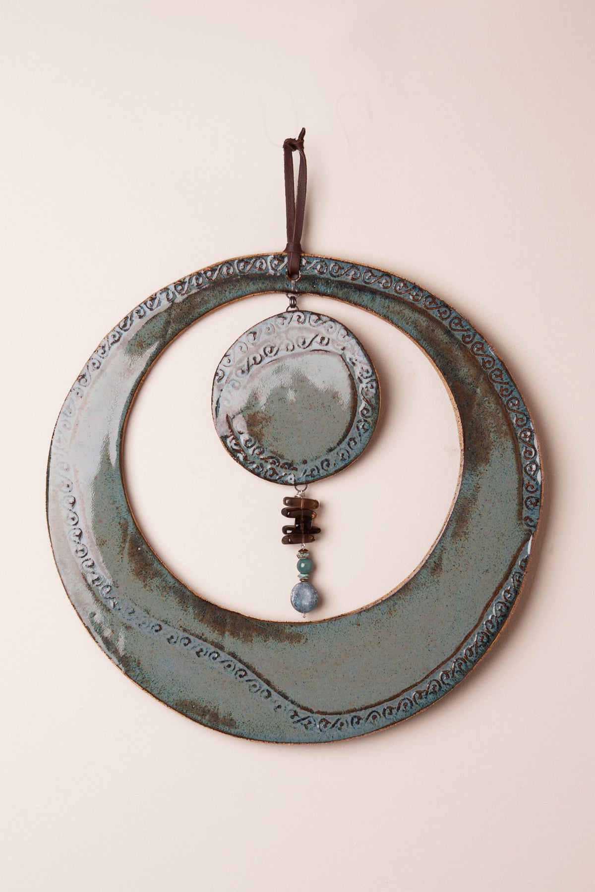 Large handmade circle ceramic wall hanging in Sea Breeze glaze with scroll pattern and kyanite, smoky topaz and aventurine dangle, kiln fired by Jester Swink Santa Cruz Mountains — From the Fire FTF_1026