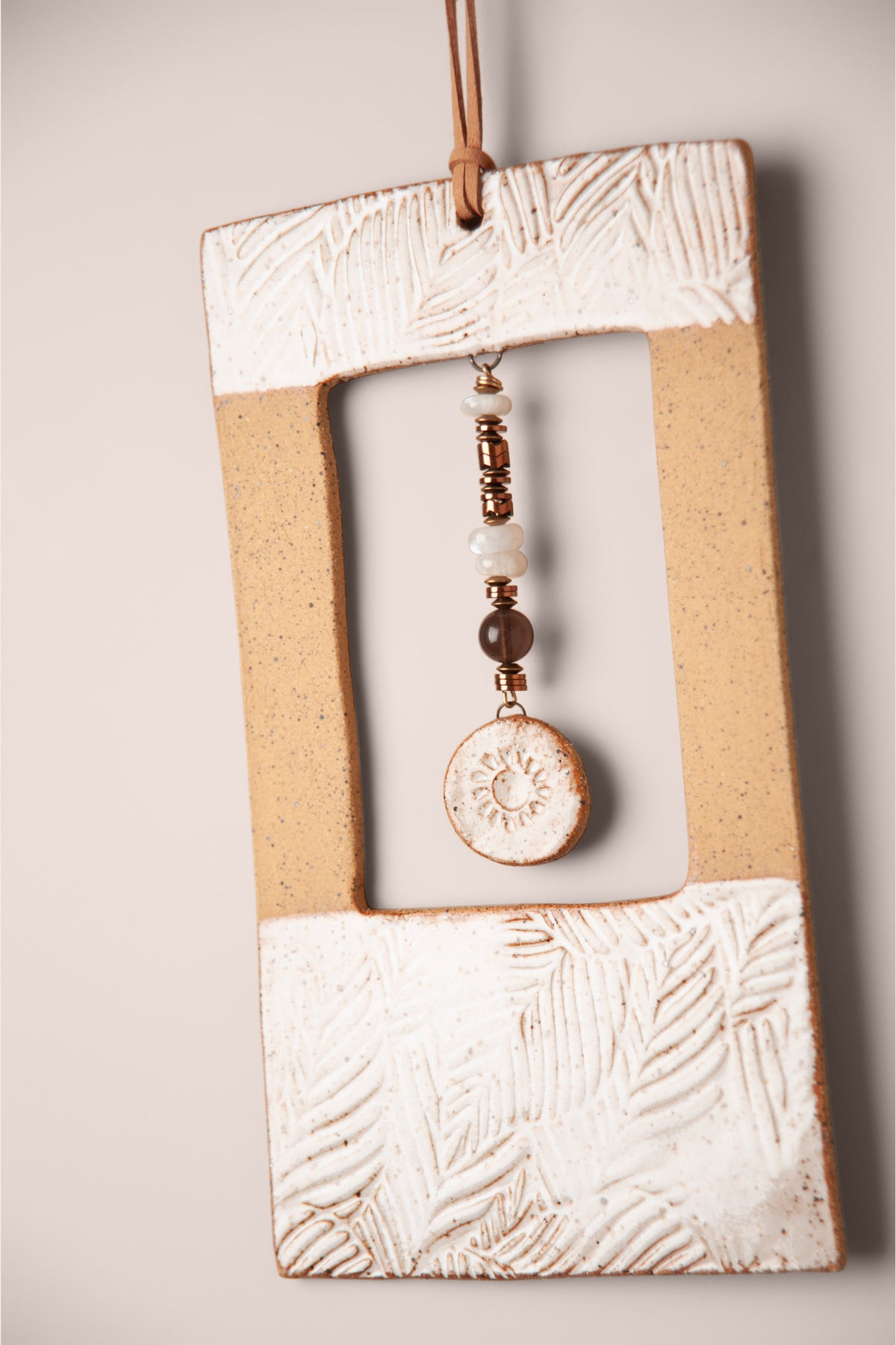 Detail of the pressed leaves and stone dangle on a large handmade rectangle ceramic wall hanging in white glaze, kiln fired by Jester Swink, Santa Cruz Mountains California