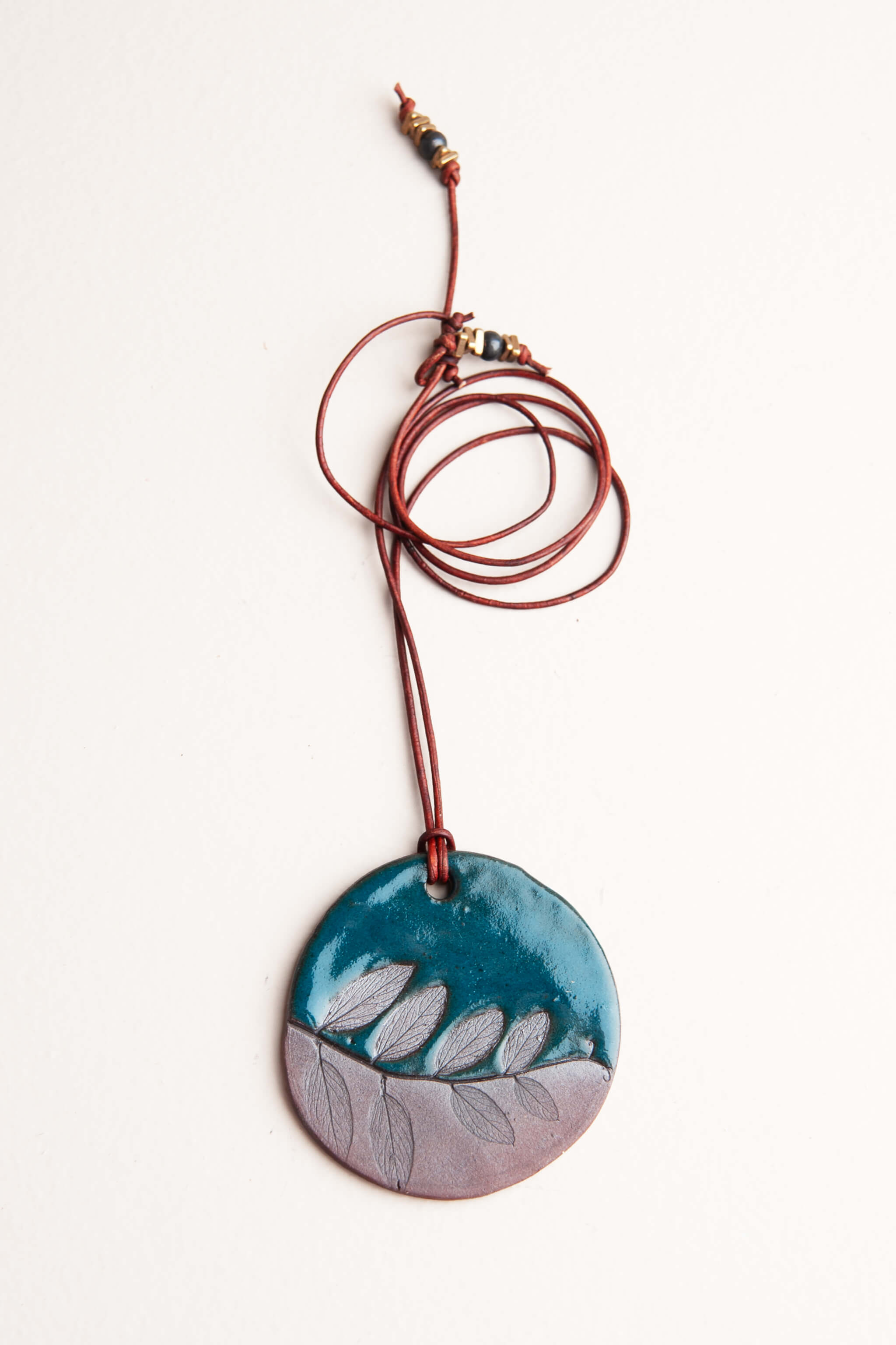 Handmade ceramic leaf impression pendant necklace in deep sea blue and raw terracotta on brown Italian leather, kiln fired by Jester Swink Santa Cruz Mountains — From the Fire FTF_0726
