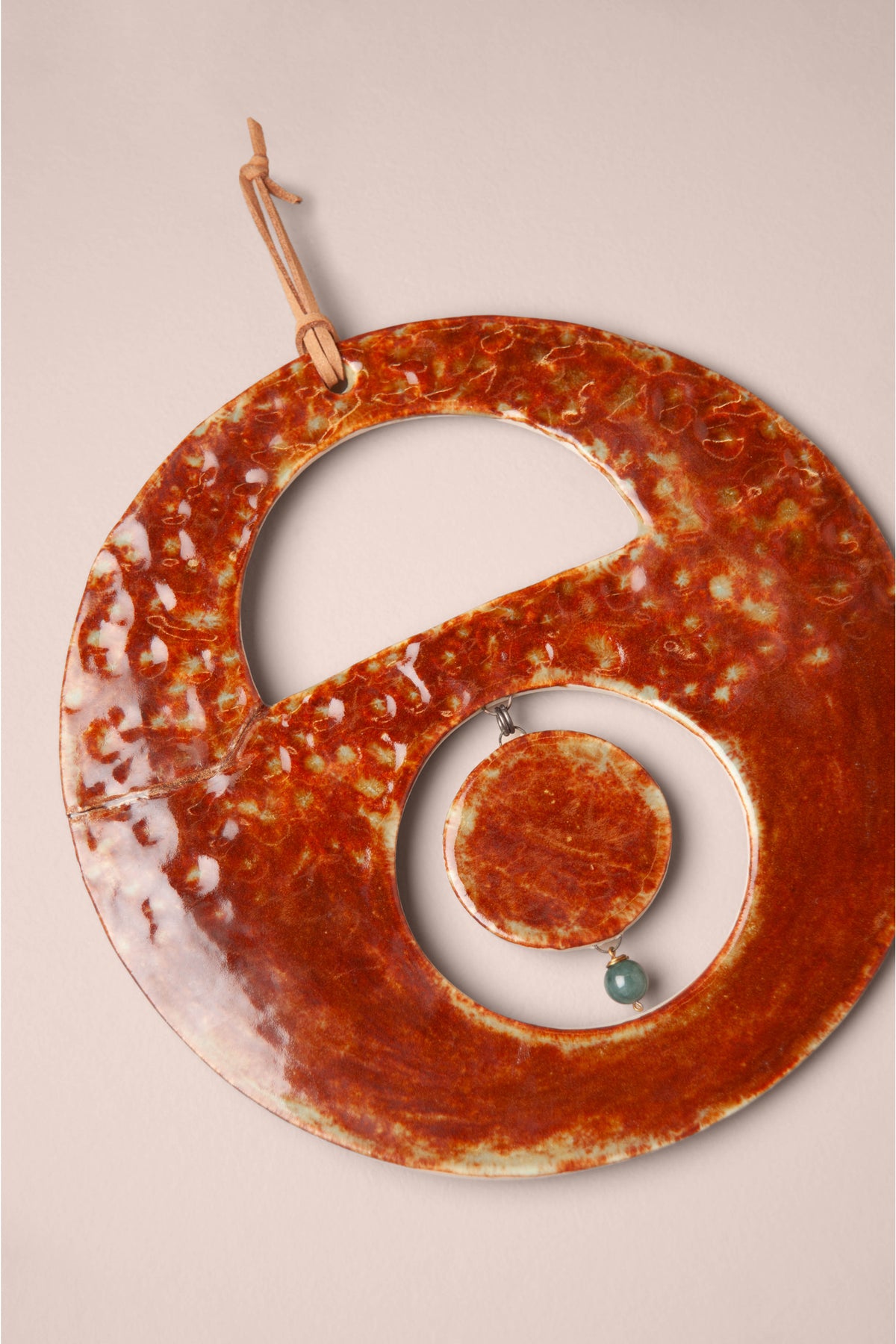 Detail of the hammered Oolong glaze and hanging moons on a medium handmade round ceramic wall hanging, kiln fired by Jester Swink, Santa Cruz Mountains California