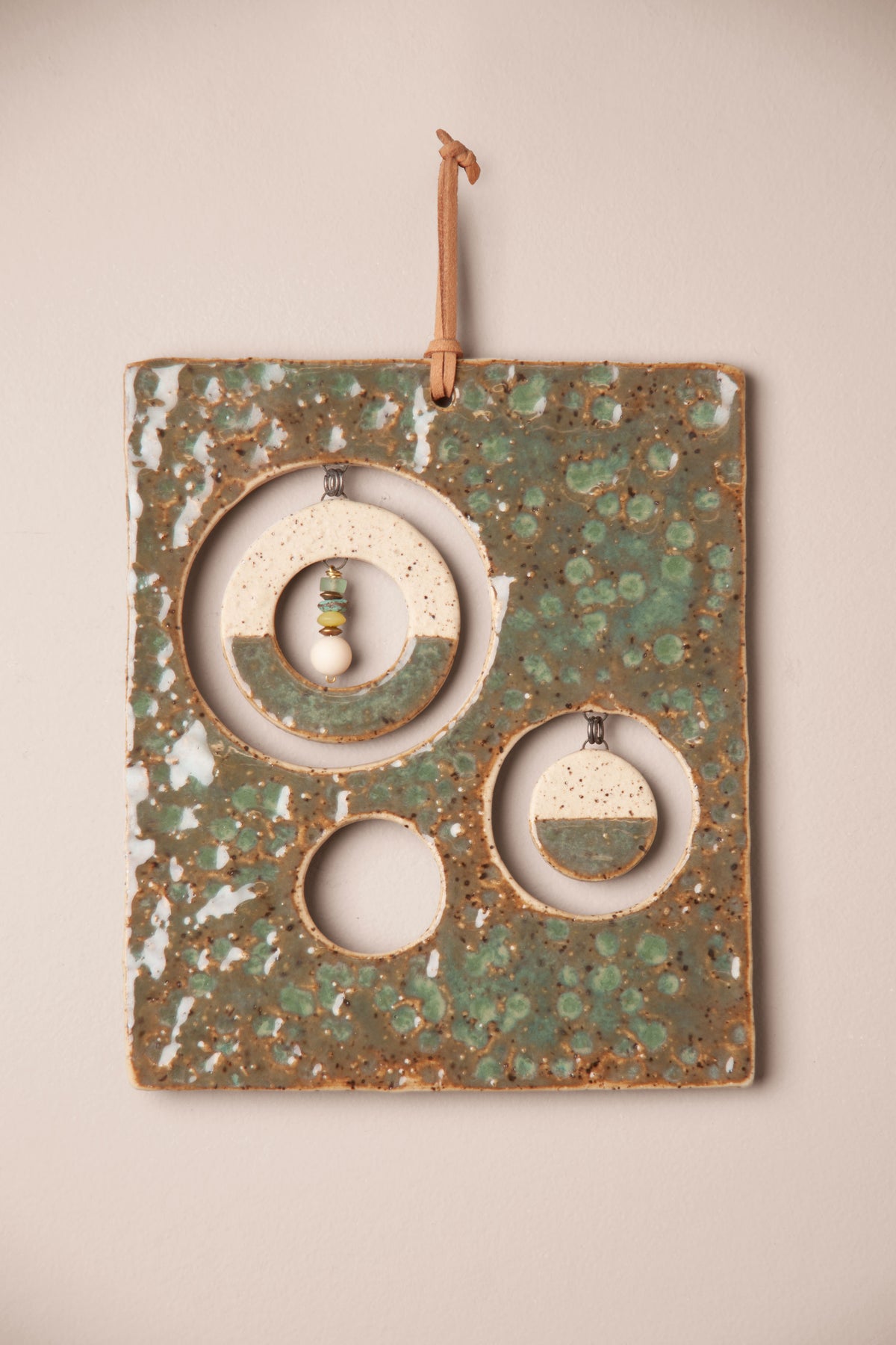 Detail of the hammered glaze, hanging moons and stones on a medium handmade rectangle ceramic wall hanging, kiln fired by Jester Swink, Santa Cruz Mountains California