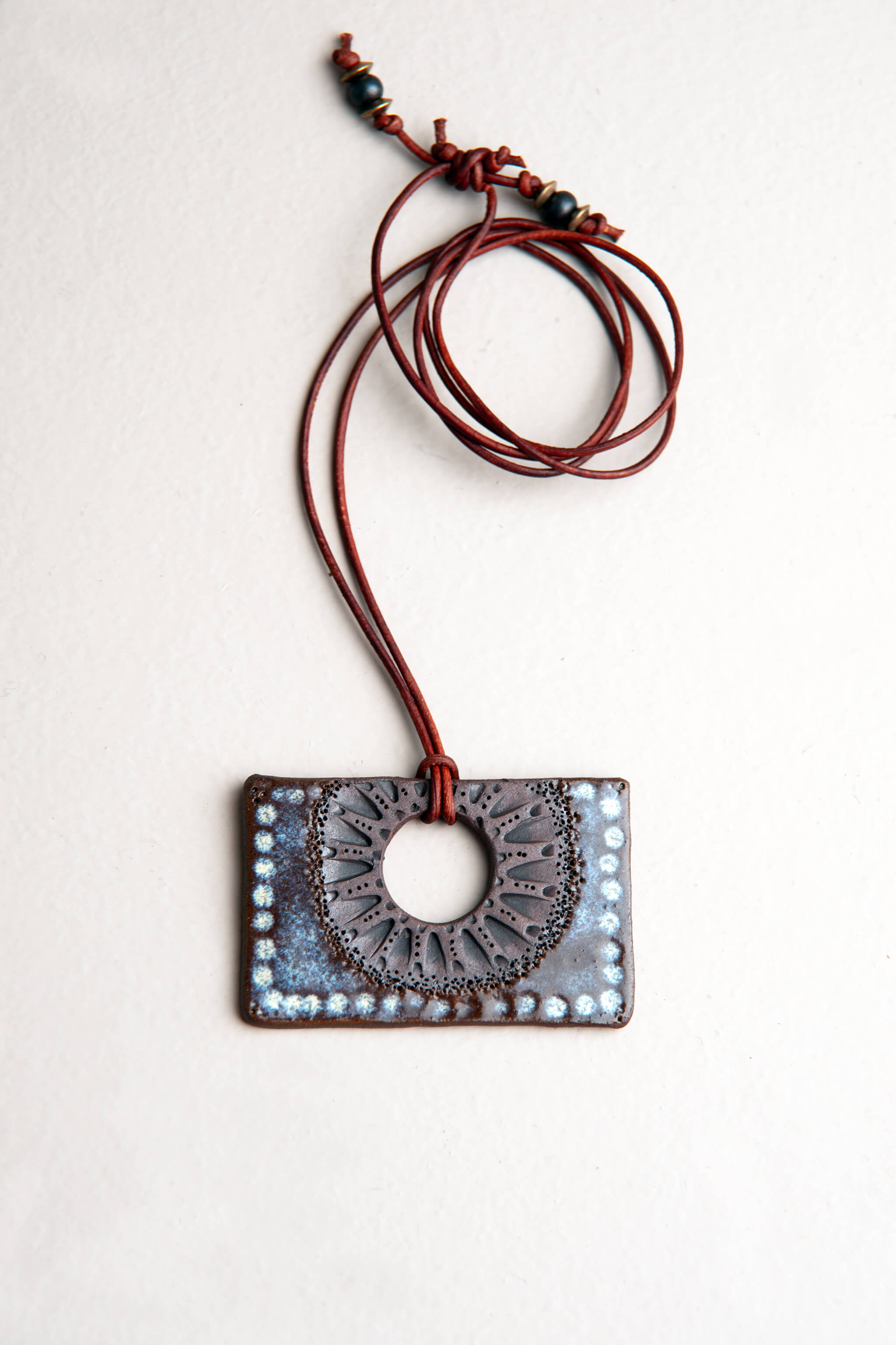 Handmade ceramic rectangle pendant necklace in raw terracotta with sea breeze glaze and sunburst pattern on dark vintage leather, kiln fired by Jester Swink Santa Cruz Mountains — From the Fire FTF_0726