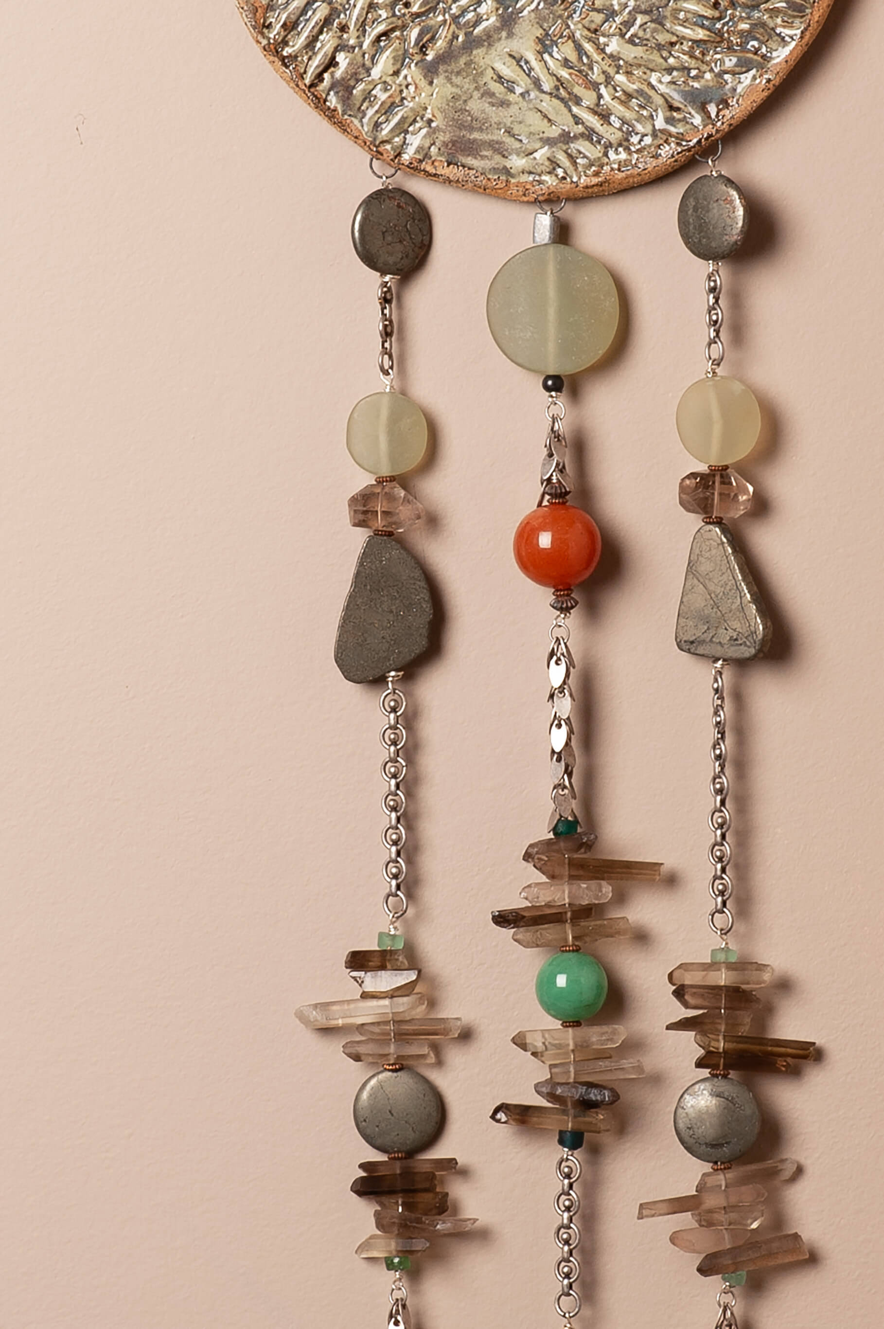 Close-up detail of hand-carved mountain peaks in sierra speckled clay with green tourmaline glaze and natural stone beads