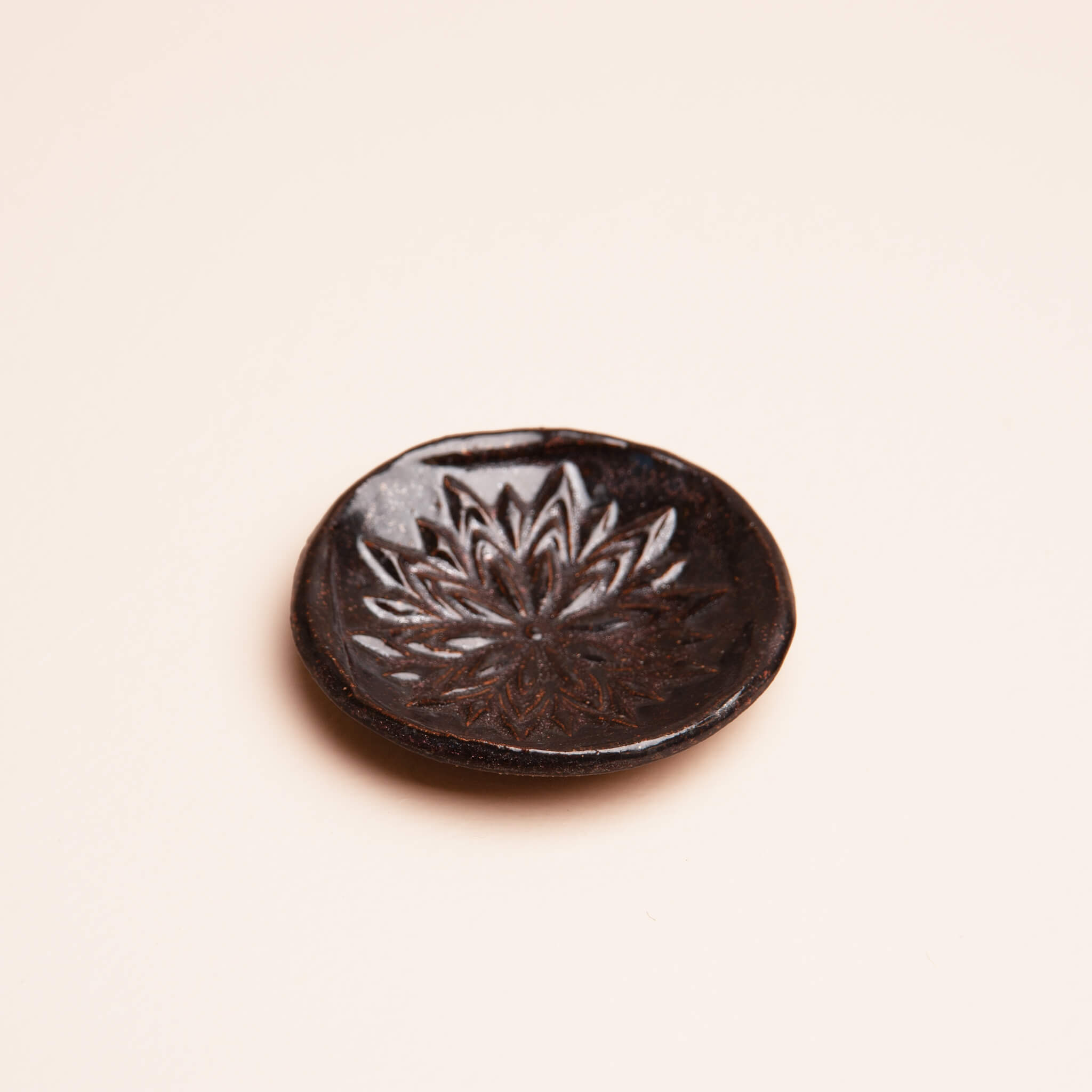 Angled view of handmade ceramic Obsidian Bloom ring dish showing depth and floral mandala stamp texture, dark metallic glaze on sierra mist clay, by Jester Swink