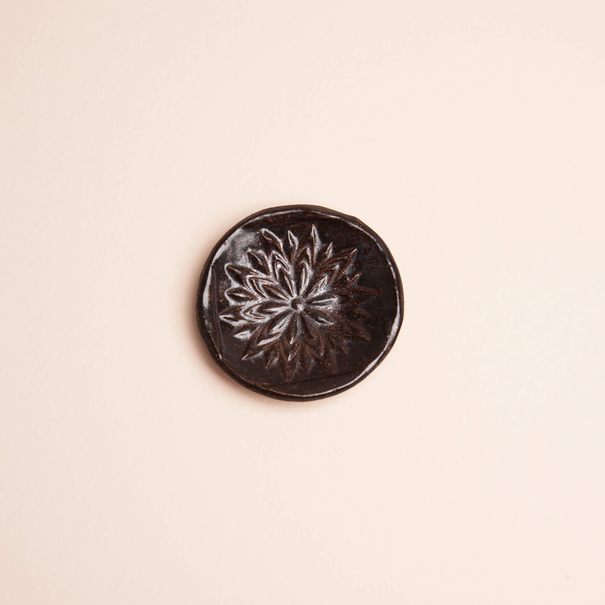 Overhead view of handmade ceramic Obsidian Bloom ring dish with deep floral mandala texture and dark metallic glaze on sierra mist clay, by Jester Swink