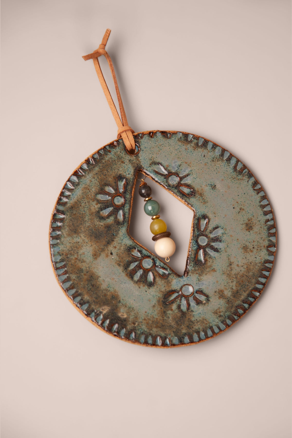 Detail of the pressed flowers and stone dangle on a small handmade round ceramic wall hanging, kiln fired by Jester Swink, Santa Cruz Mountains California
