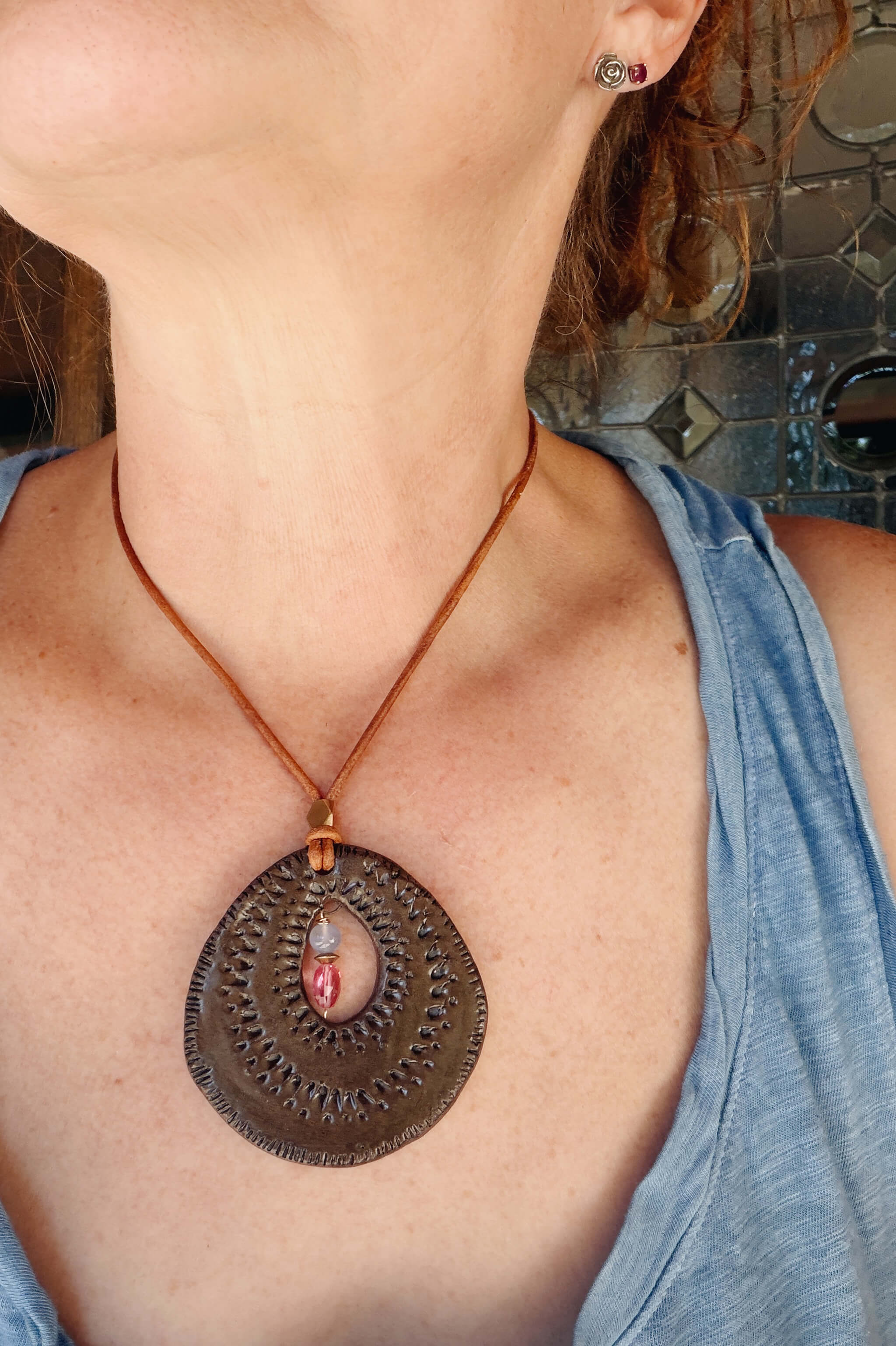 Handmade ceramic sunburst pendant necklace in chocolate brown worn on chest with rubelite and chalcedony — From the Fire FTF_0726 by Jester Swink