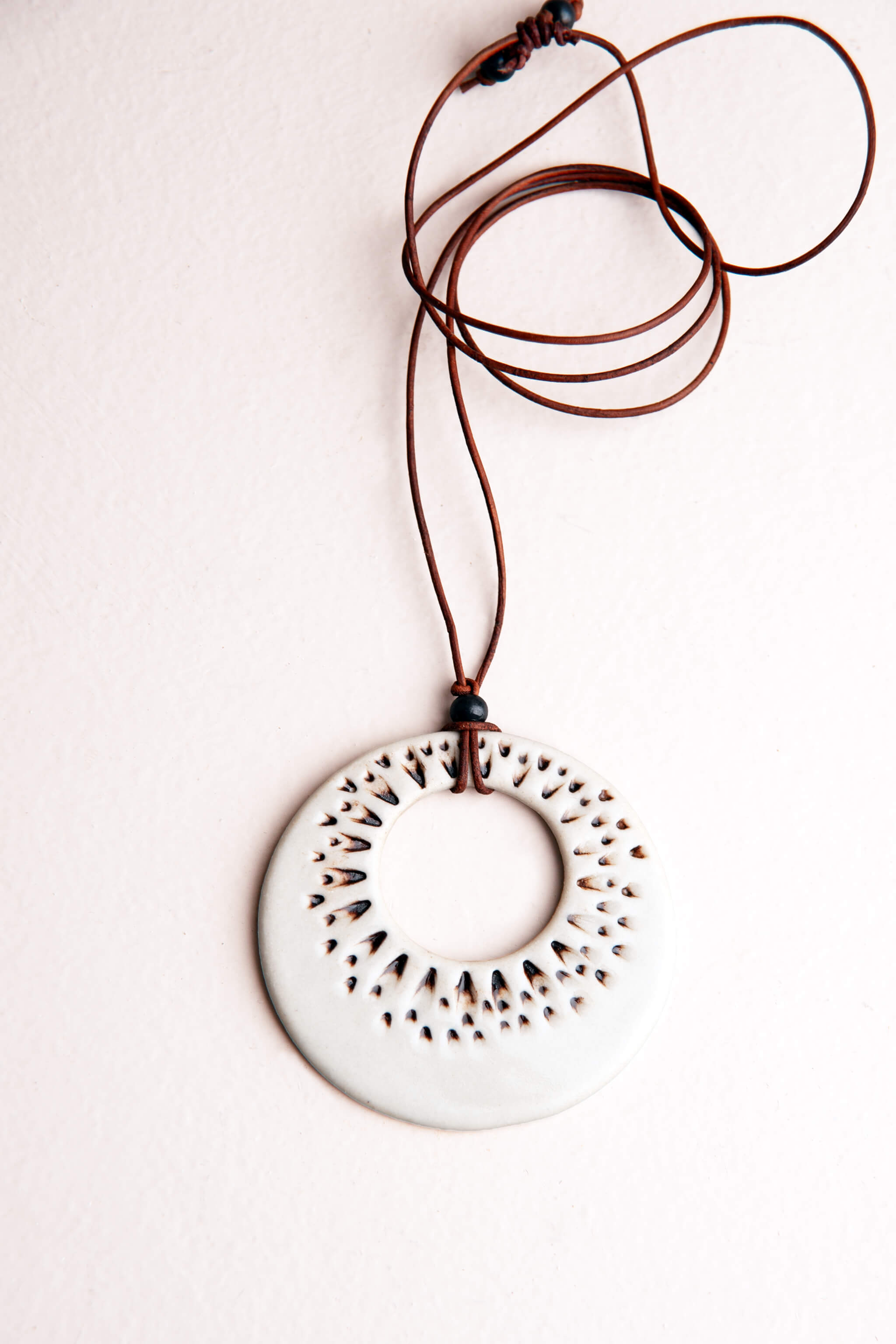 Handmade ivory porcelain sunburst ring ceramic pendant necklace with brown underglaze and oxidized brass on dark Italian leather, kiln fired by Jester Swink Santa Cruz Mountains — From the Fire FTF_0726
