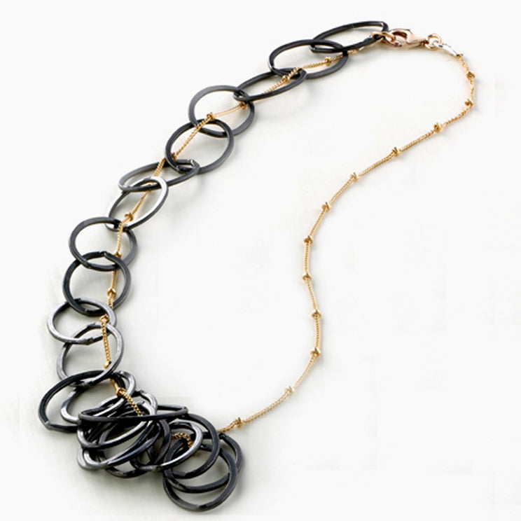 Bold oxidized mixed metal asymmetrical necklace with dark sterling silver and 14K gold fill chains, shown as a statement piece.