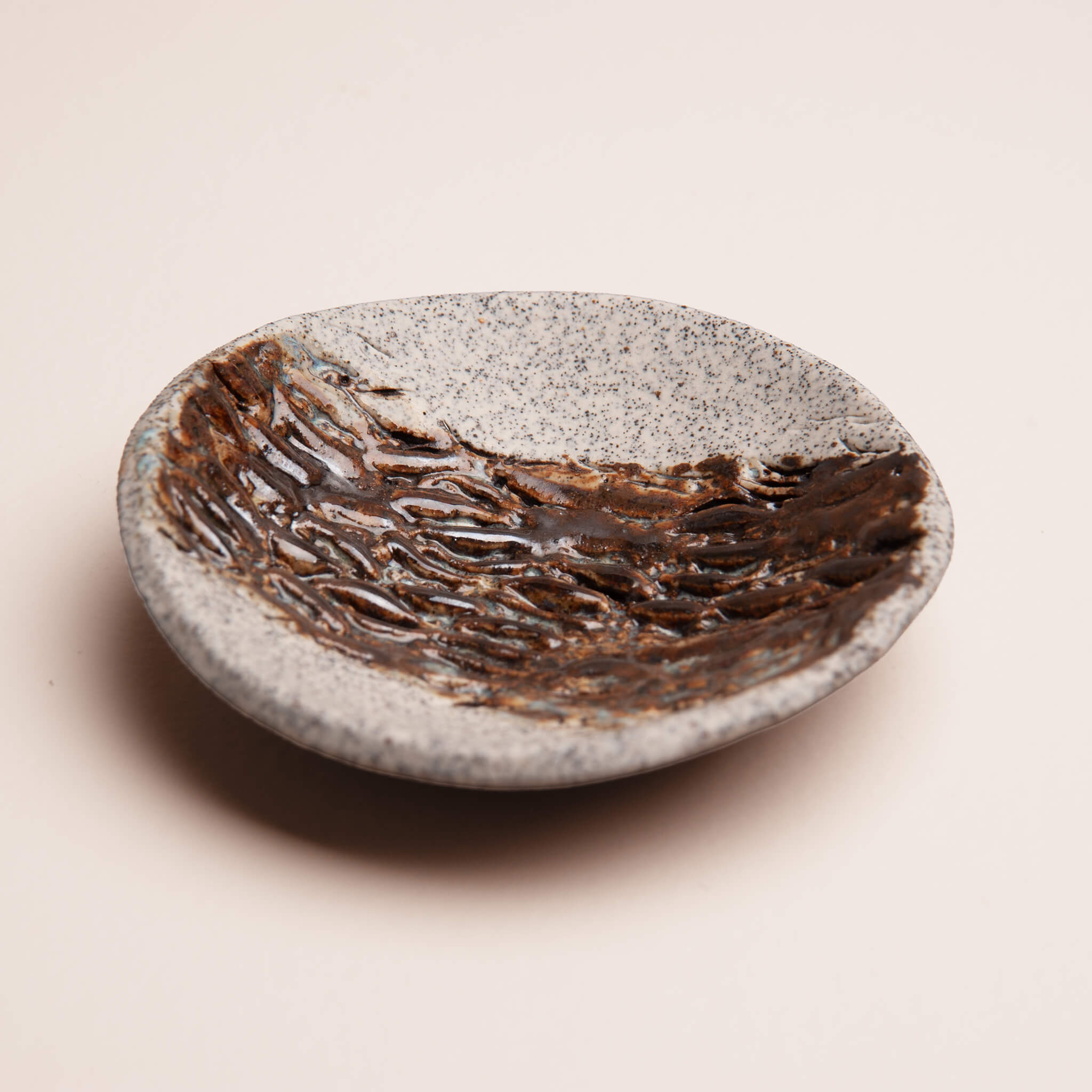 Alt text: Angled view of handmade ceramic Banksia Pod ring dish showing depth and organic texture, brown glaze with ice blue accents, dragon fruit clay, by Jester Swink