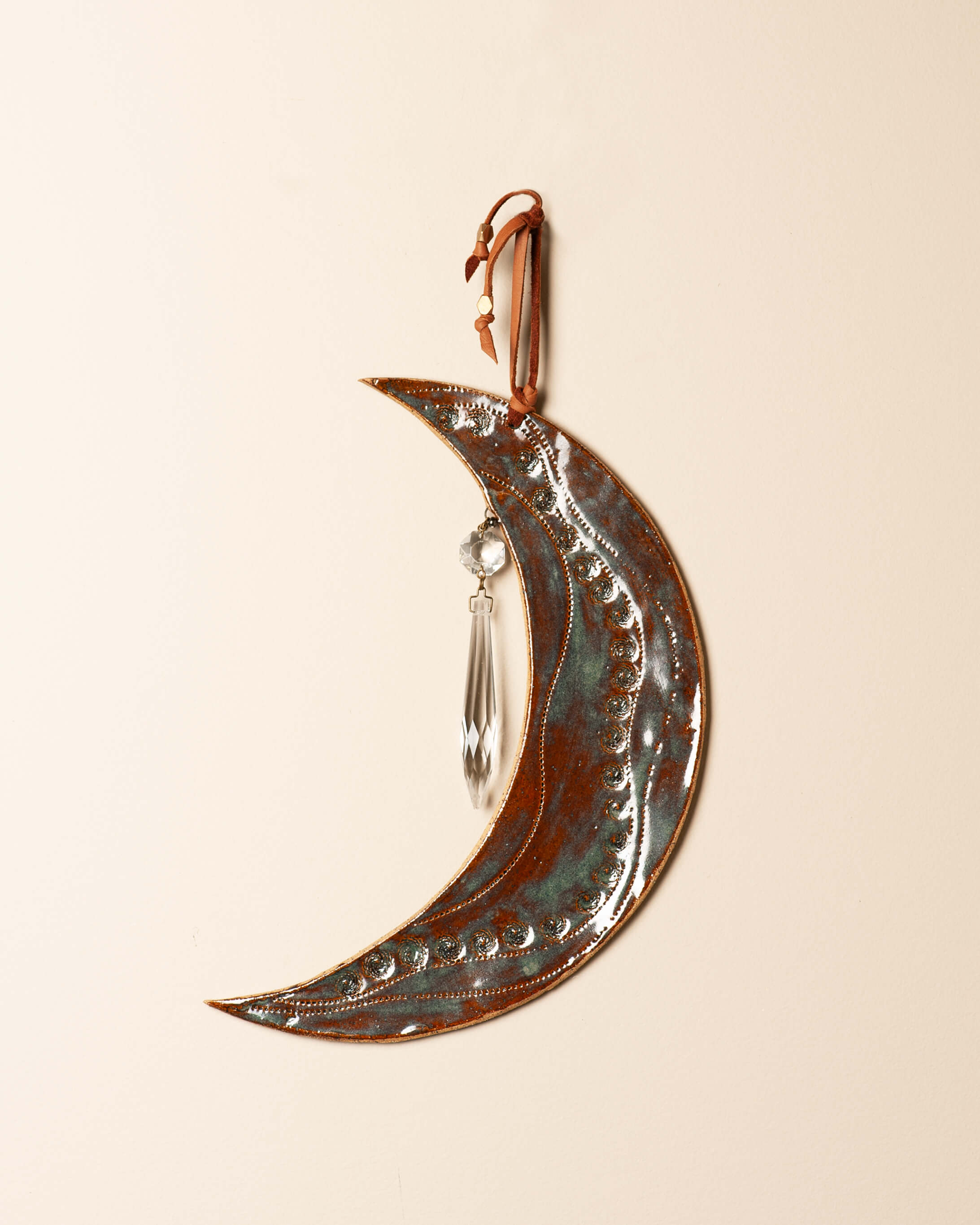 Handcrafted crescent moon wall hanging in ceramic clay with copper and teal glaze, antique crystal drop, and leather hanger — Jester Swink