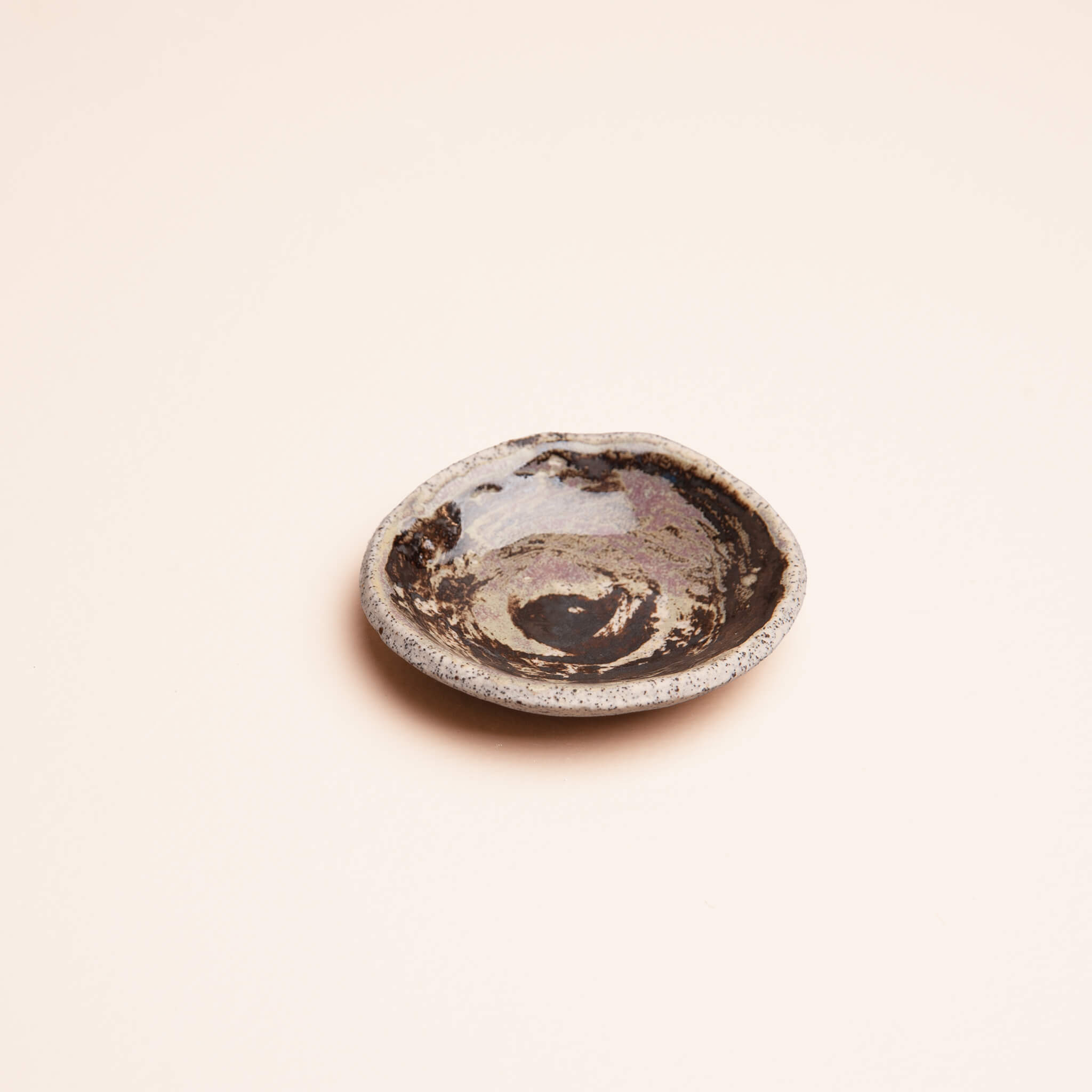 Angled view of handmade ceramic Galaxy Swirl ring dish with swirling brown copper and lavender glaze on dragon fruit clay, by Jester Swink