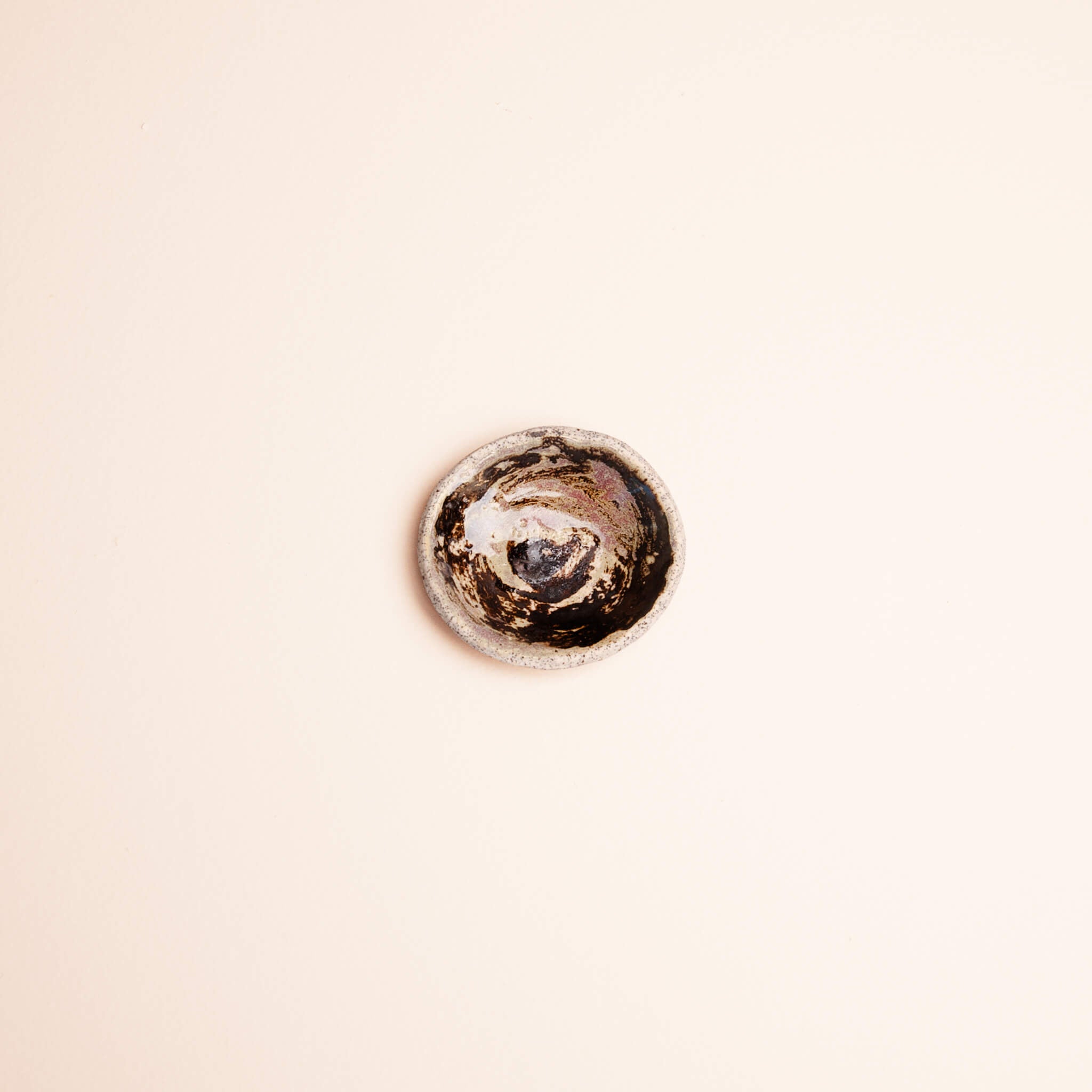 Overhead view of handmade ceramic Galaxy Swirl ring dish showing swirling motion of brown copper and lavender glaze, dragon fruit clay, by Jester Swink