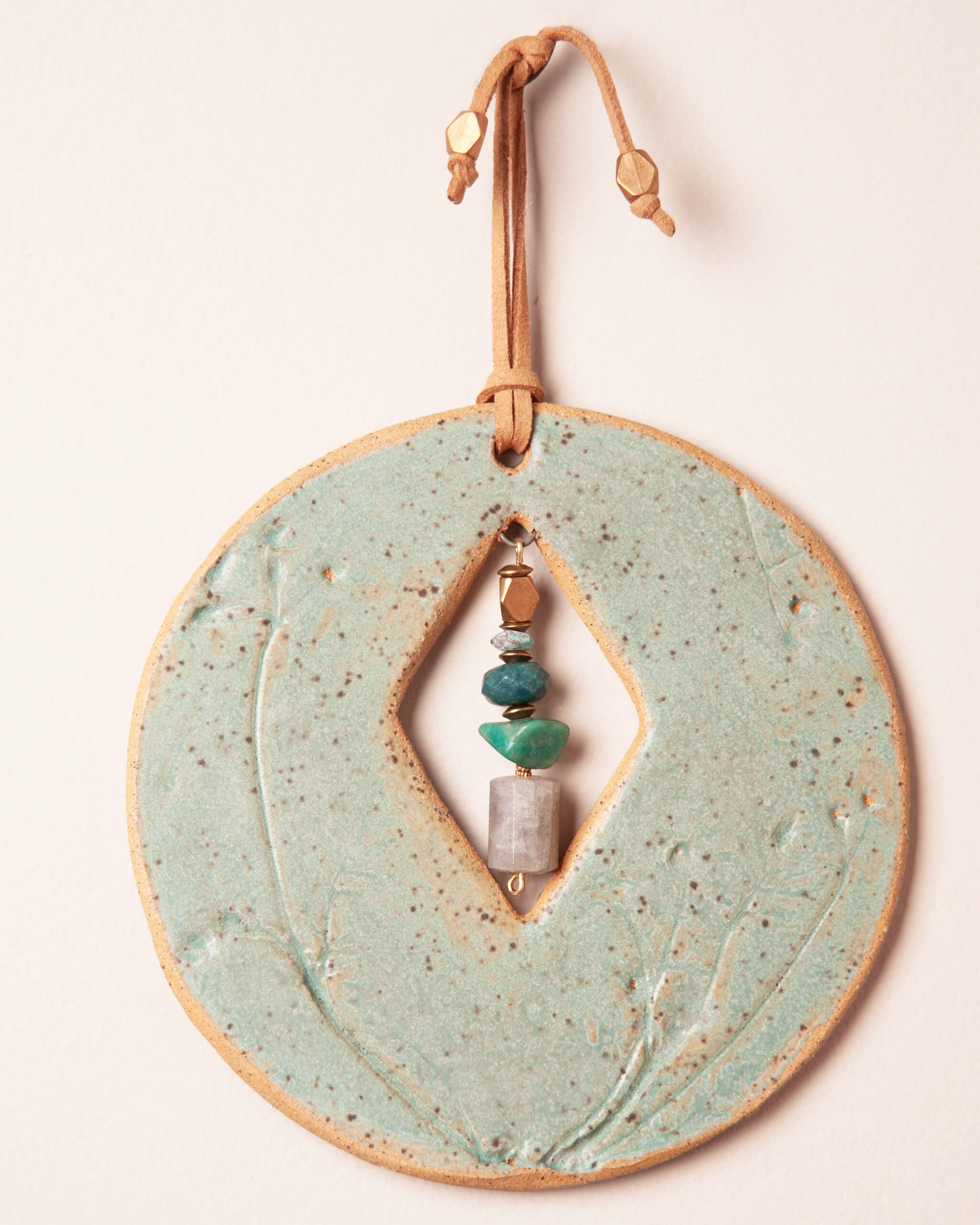 Close up of wildflower stork's bill impression in seafoam green glazed ceramic clay with light tan leather and bronze accents