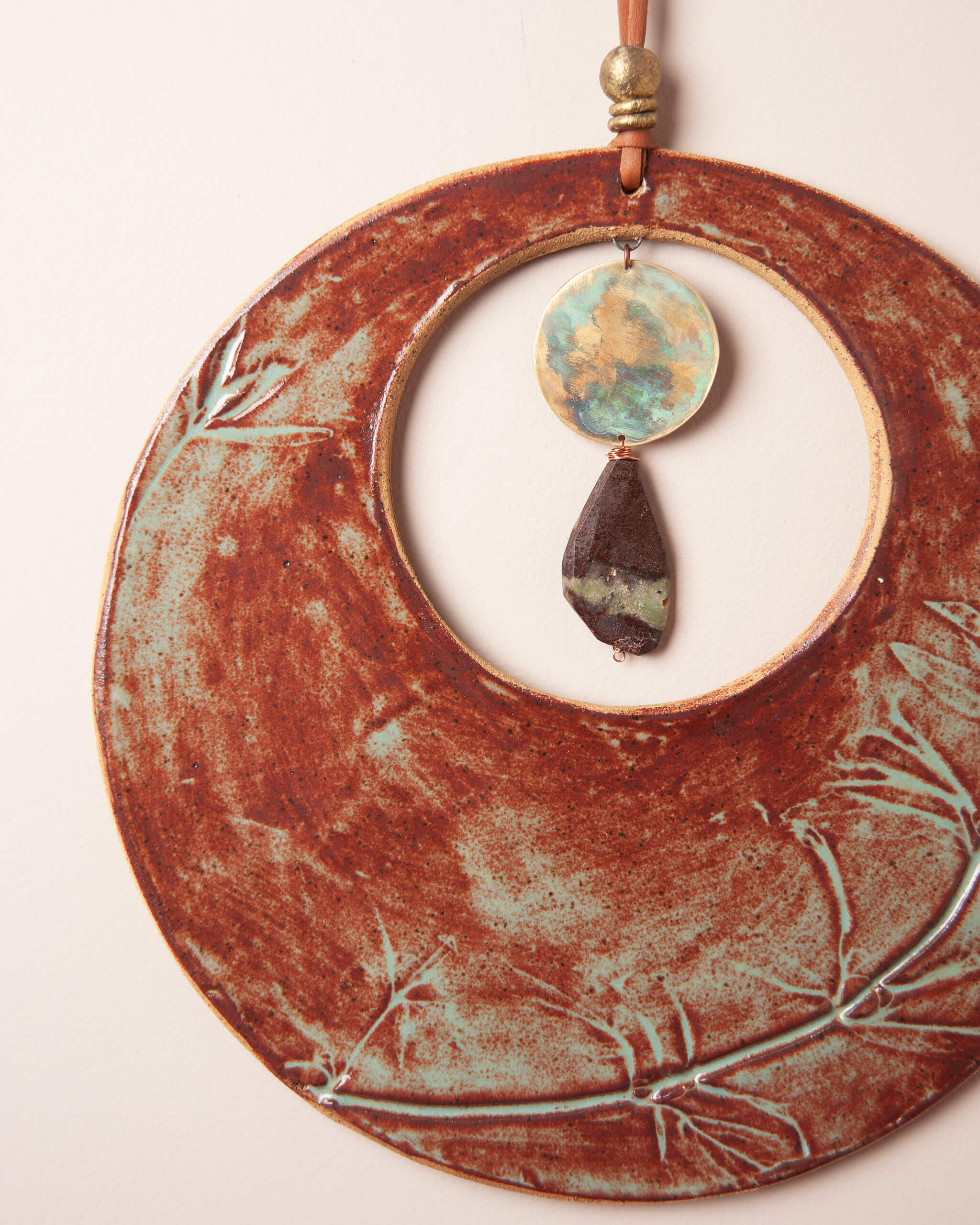 Close up of monkey flower impression in rusty terracotta glazed river rock ceramic clay with hand patinated brass disc and chrysoprase pendant