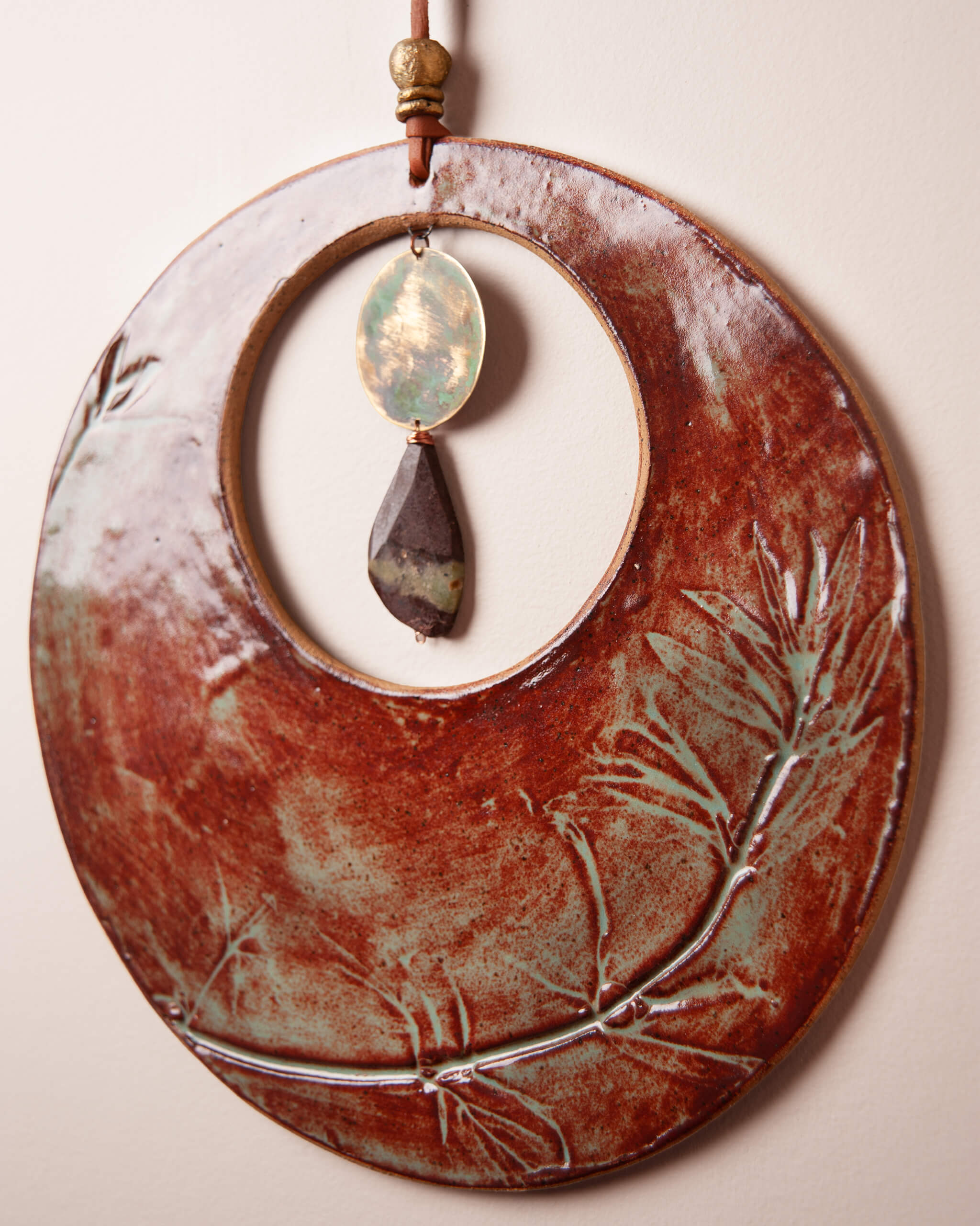 Close up of hand patinated brass disc showing copper gold and green oxidation detail with chrysoprase drop and brass accents on Crescent Blood Moon ceramic wall hanging