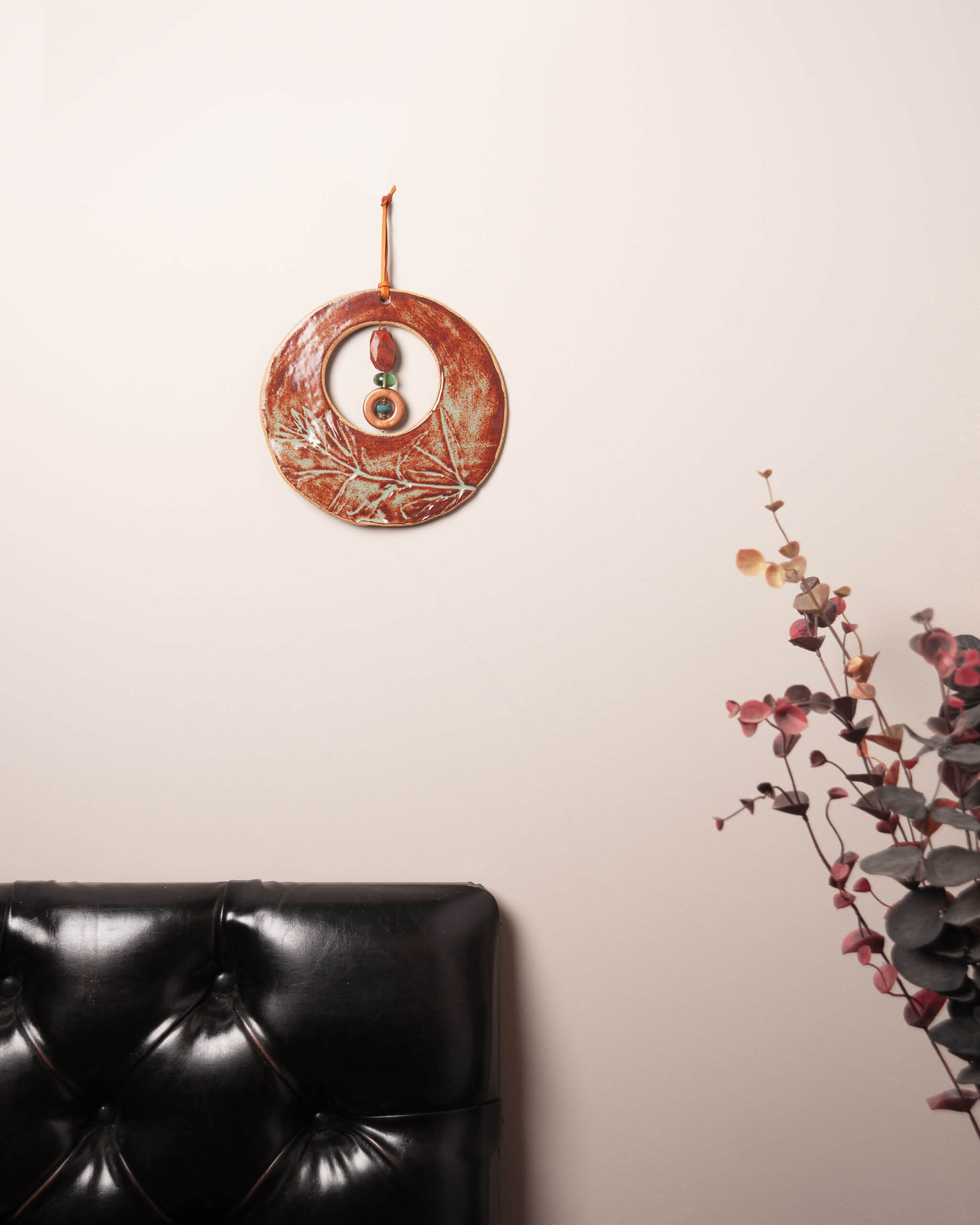 Ember Moon ceramic wall hanging displayed in home setting showing warm rusty orange and sage glaze with wildflower impression detail