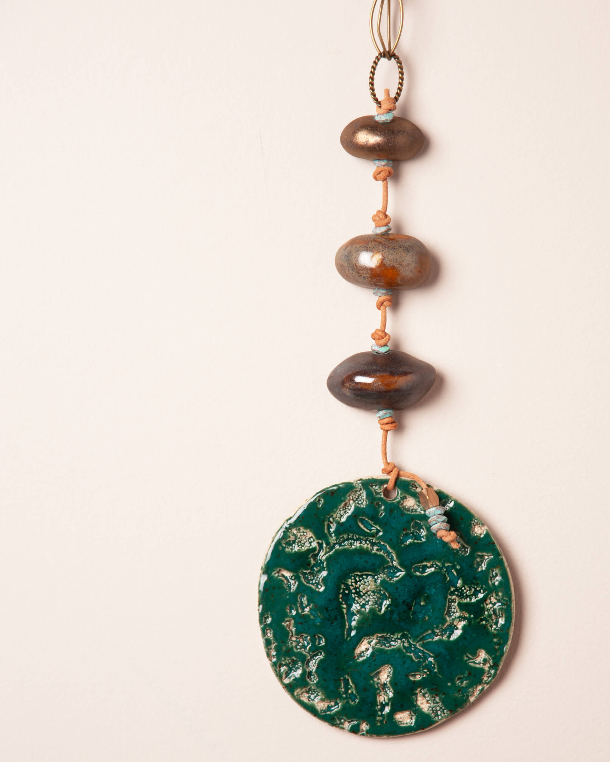 Close up of coral and abalone texture impression in deep emerald glazed white speckled ceramic disc with river rock forms and patinated brass beads