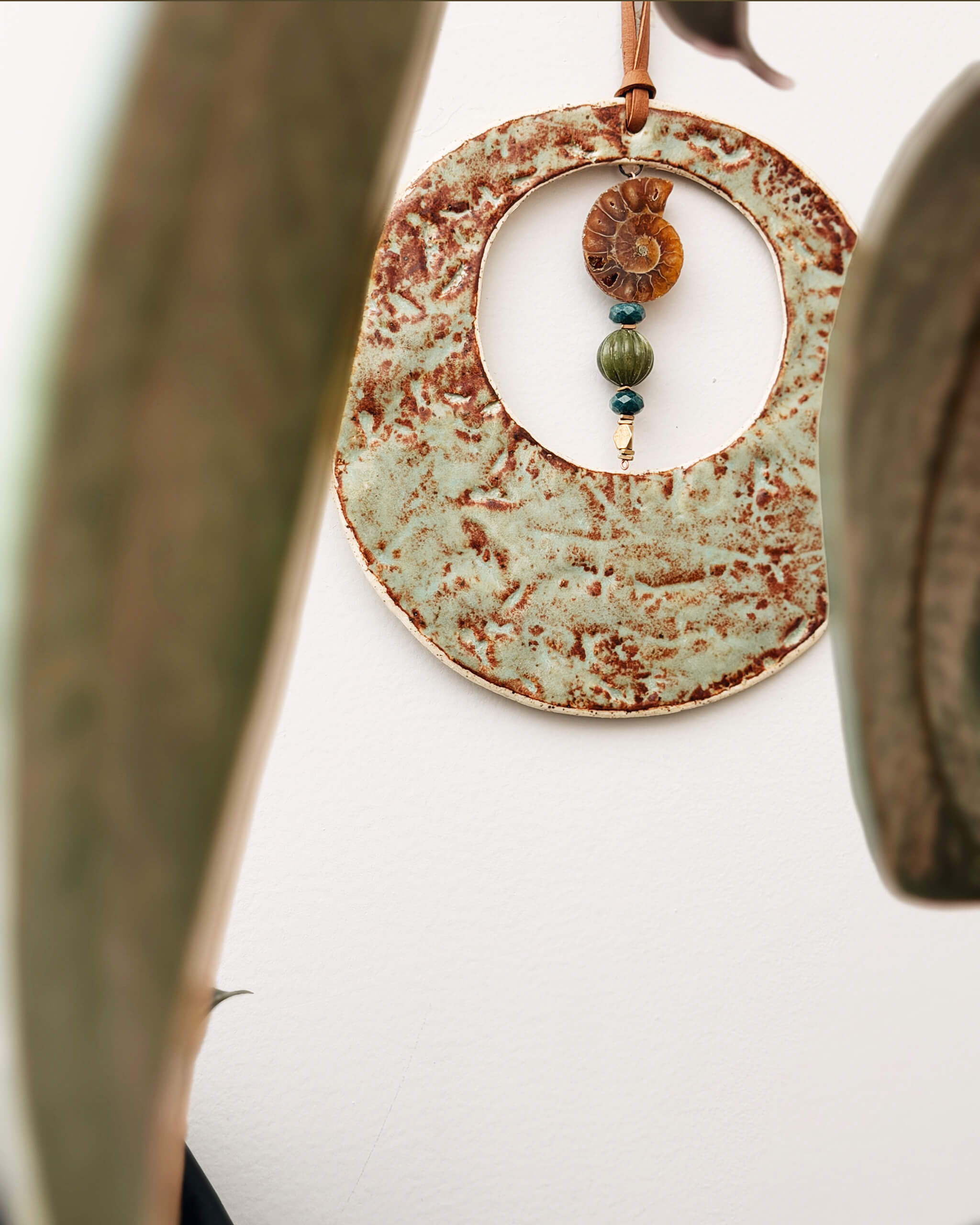 Fossil Moon ceramic wall hanging displayed on white wall with botanical framing