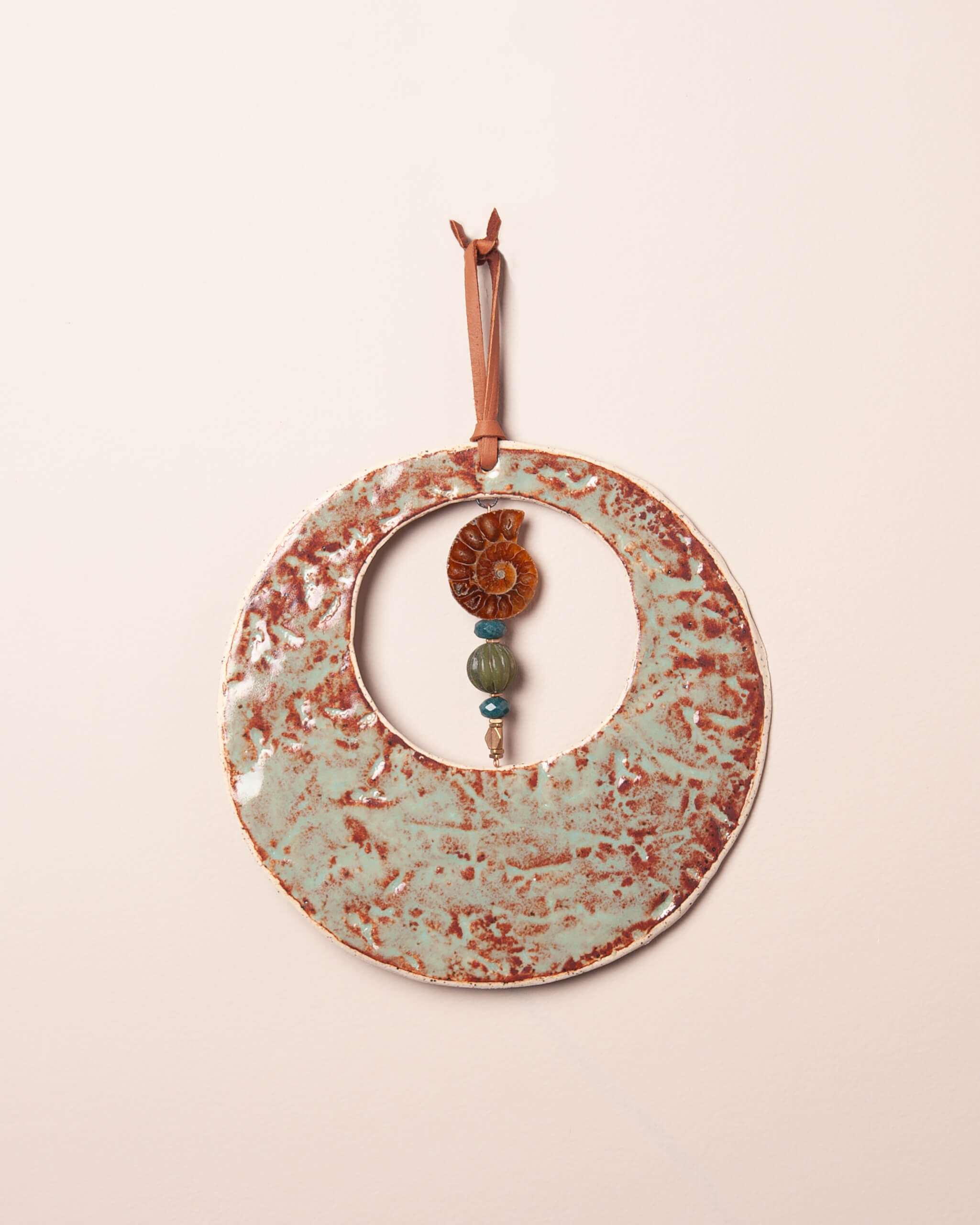 Fossil Moon handmade ceramic wall hanging with redwood bark impression, sage and rust glaze, and ammonite fossil pendant, made in the Santa Cruz Mountains of California
