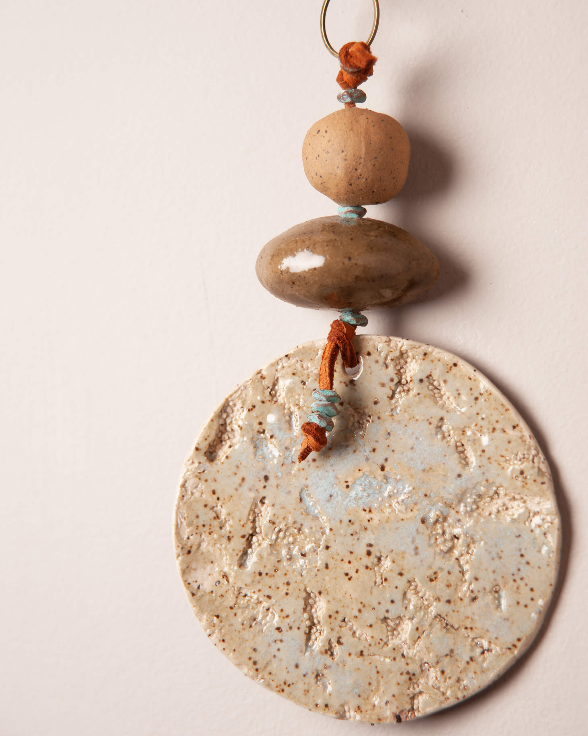 Close up of abalone and coral texture impression on ice blue glazed white speckled ceramic disc with olive green river rock bead and patinated brass accents