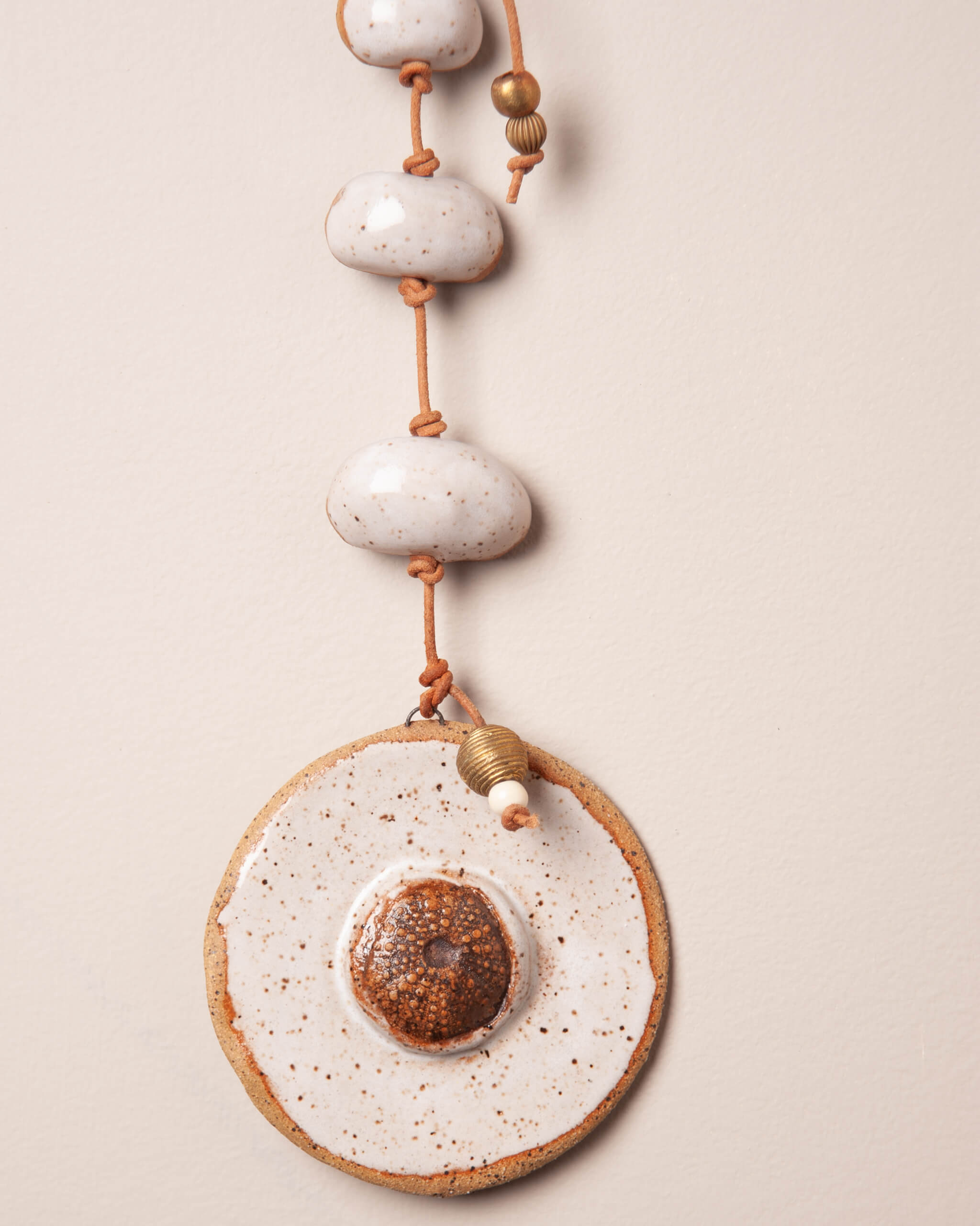 Close up of Moroccan fossil sea urchin impression raised above white frost glazed ceramic disc with river rock stack and brass accents