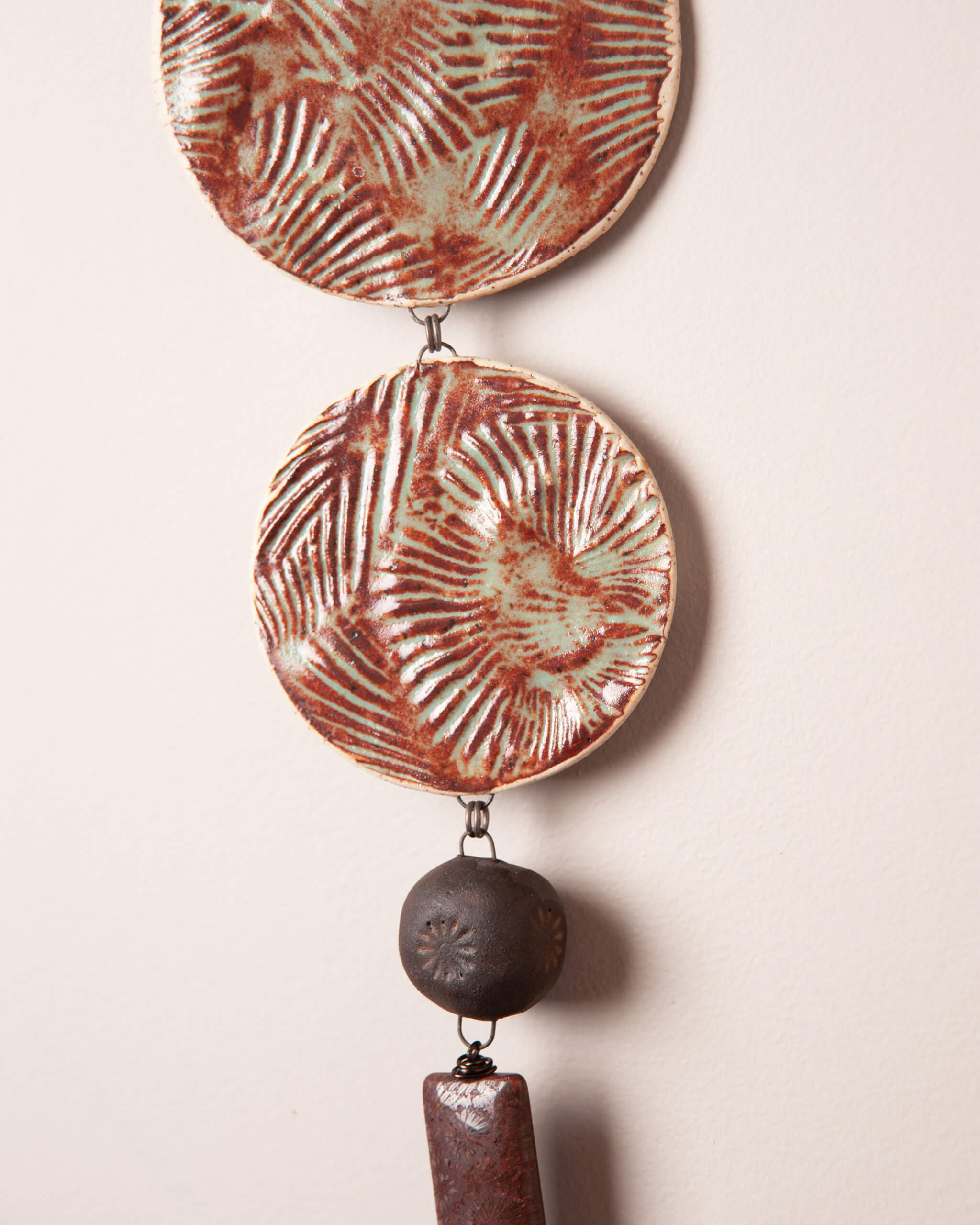 Close up of shell texture impression on rusty terracotta glazed white speckled ceramic discs with dark night clay flower stamped bead and fossilized coral agate